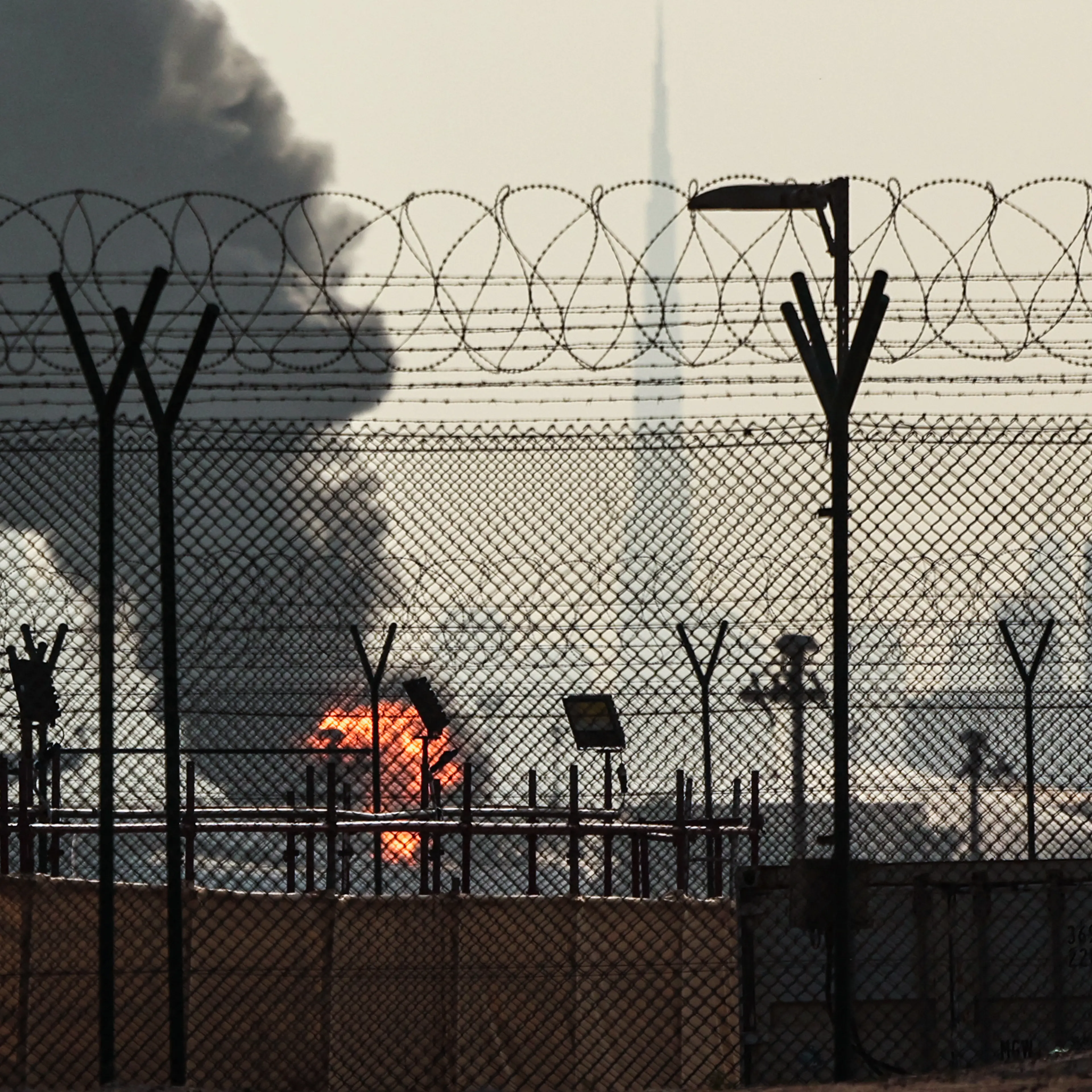 The Dubai skyline with the landmark Burj Khalifa skyscraper (R) is pictured as a smoke plume rises from an ongoing fire near Dubai International Airport on March 16, 2026.