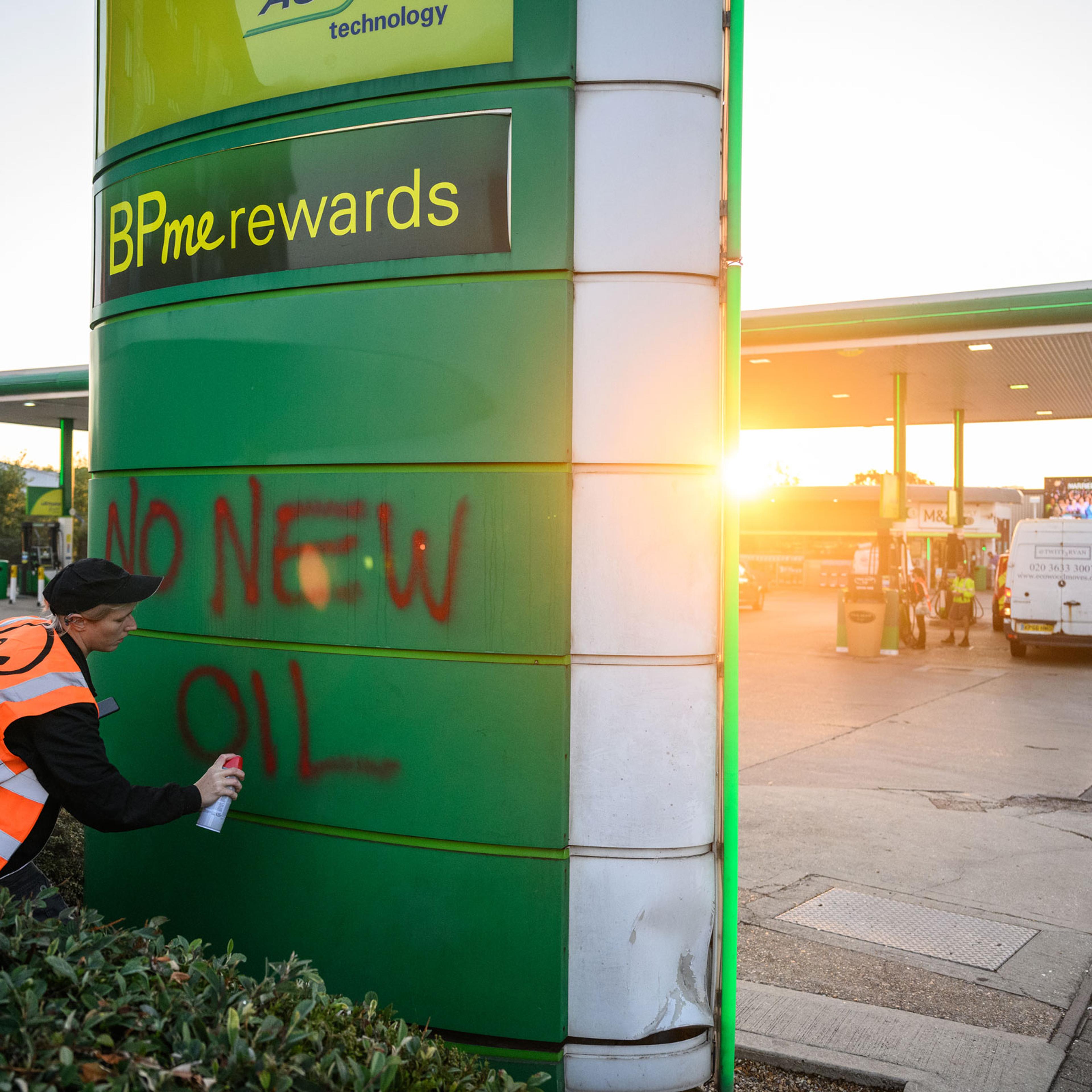 A woman sprays a message reading “No New Oil” on a sign outside a BP petrol station