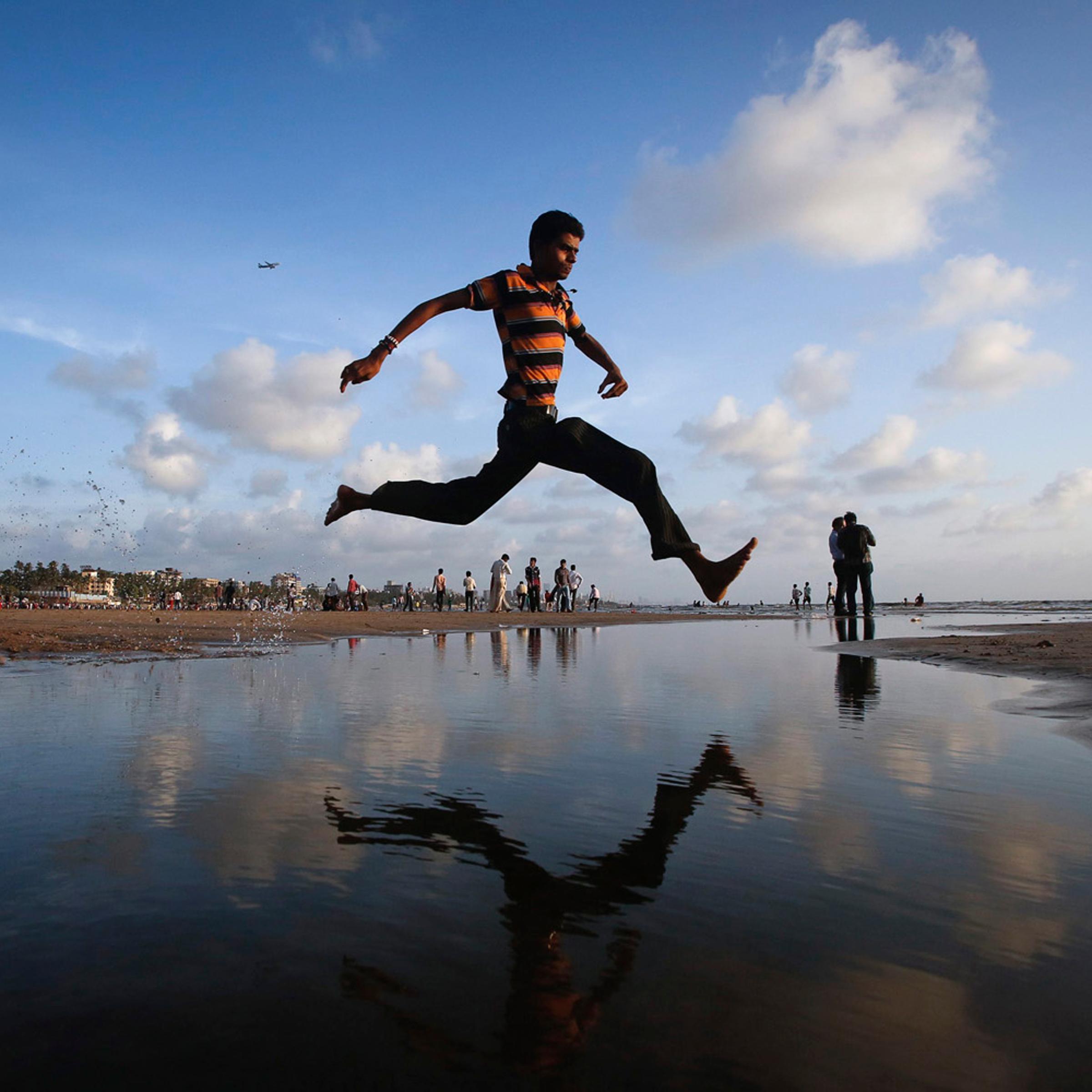 A man jumps over a water stream on a beach along the Arabian Sea in Mumbai