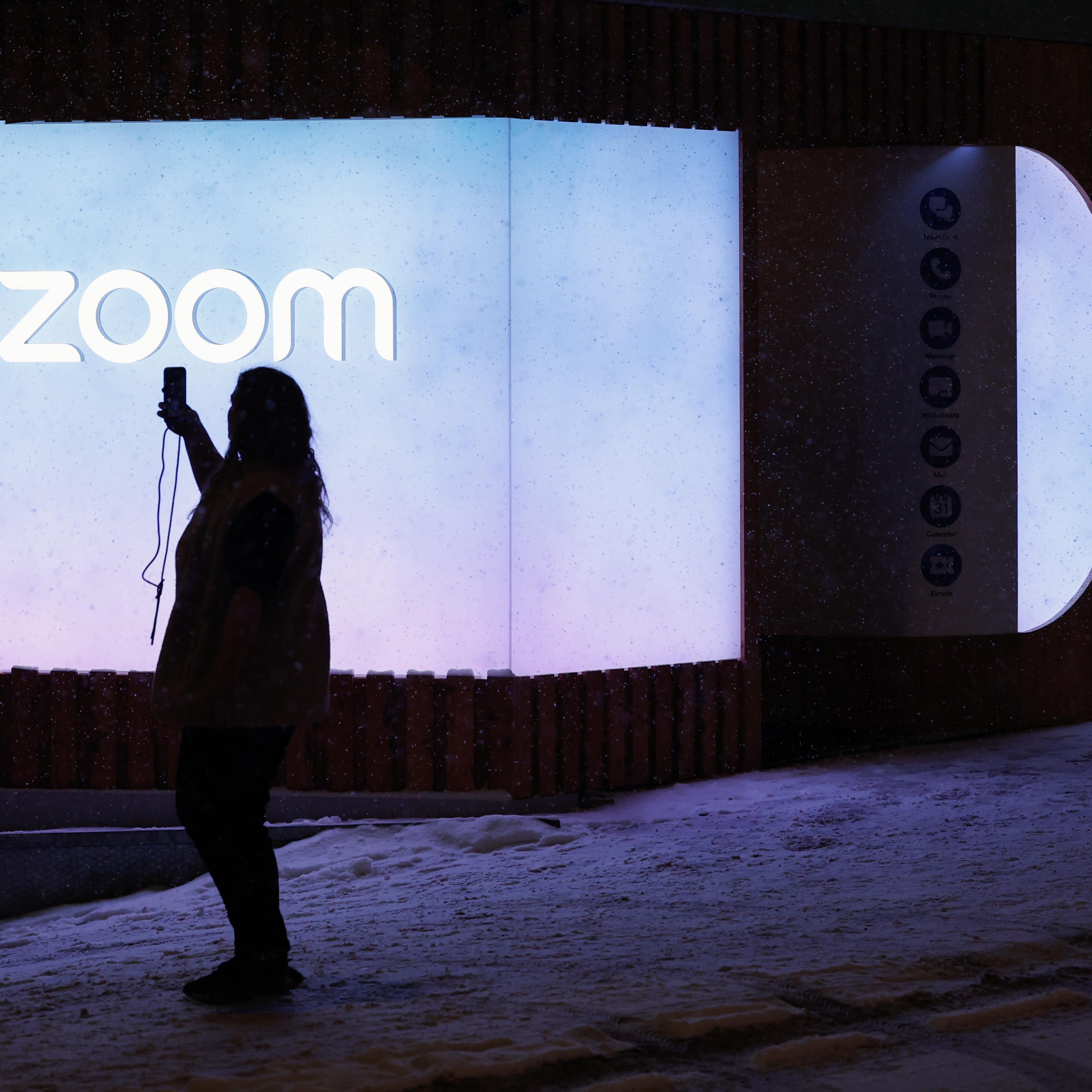 A silhouetted person poses in front of a Zoom sign
