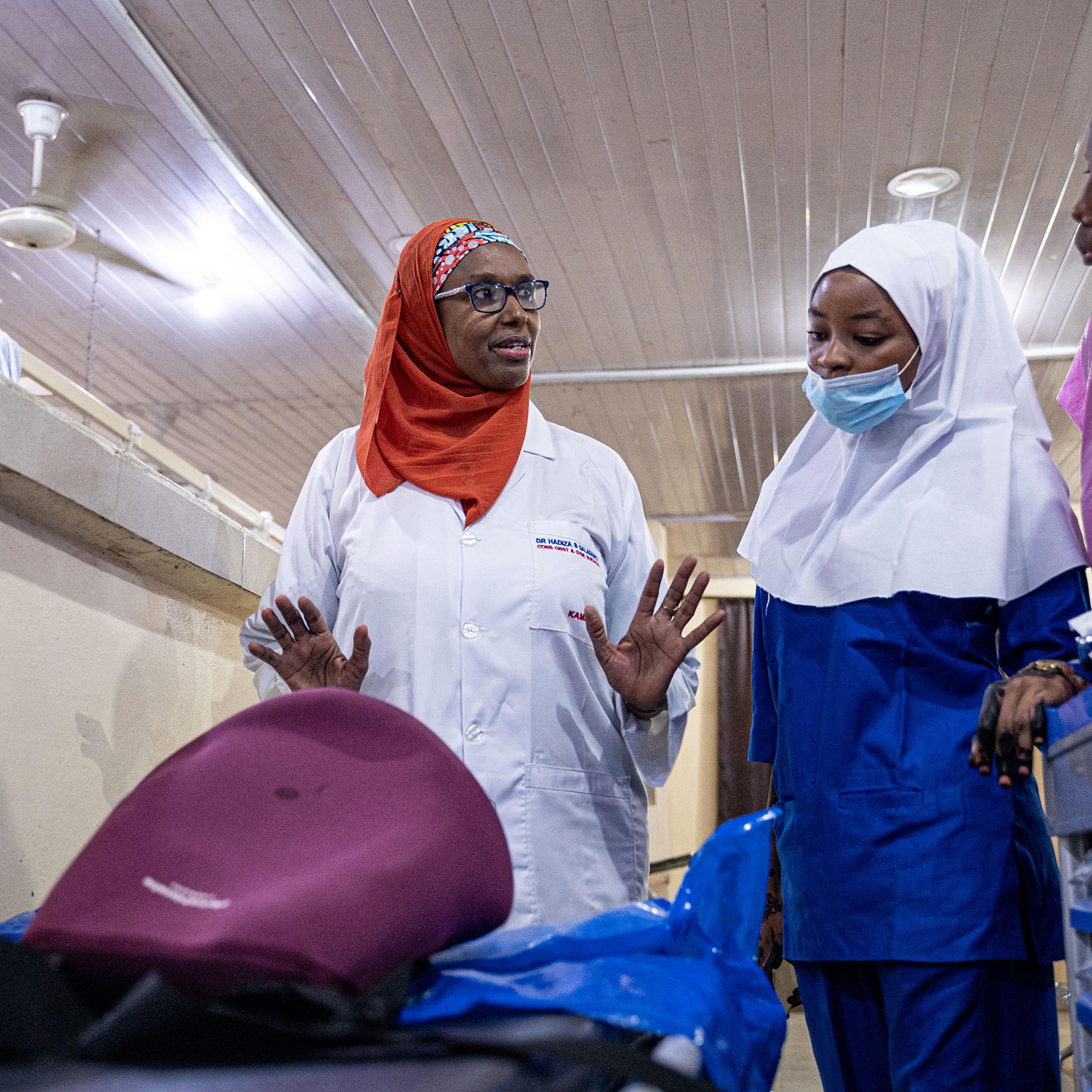Professor Hadiza Shehu Galadanci, Director of The African Center of Excellence for Population Health and Policy (ACEPHAP), demonstrates the use of the E-MOTIVE care bundle to Fatimah Sarikin Fulani (blue PPE) and Nafisa Abbas (pink) in the E-MOVITE resea