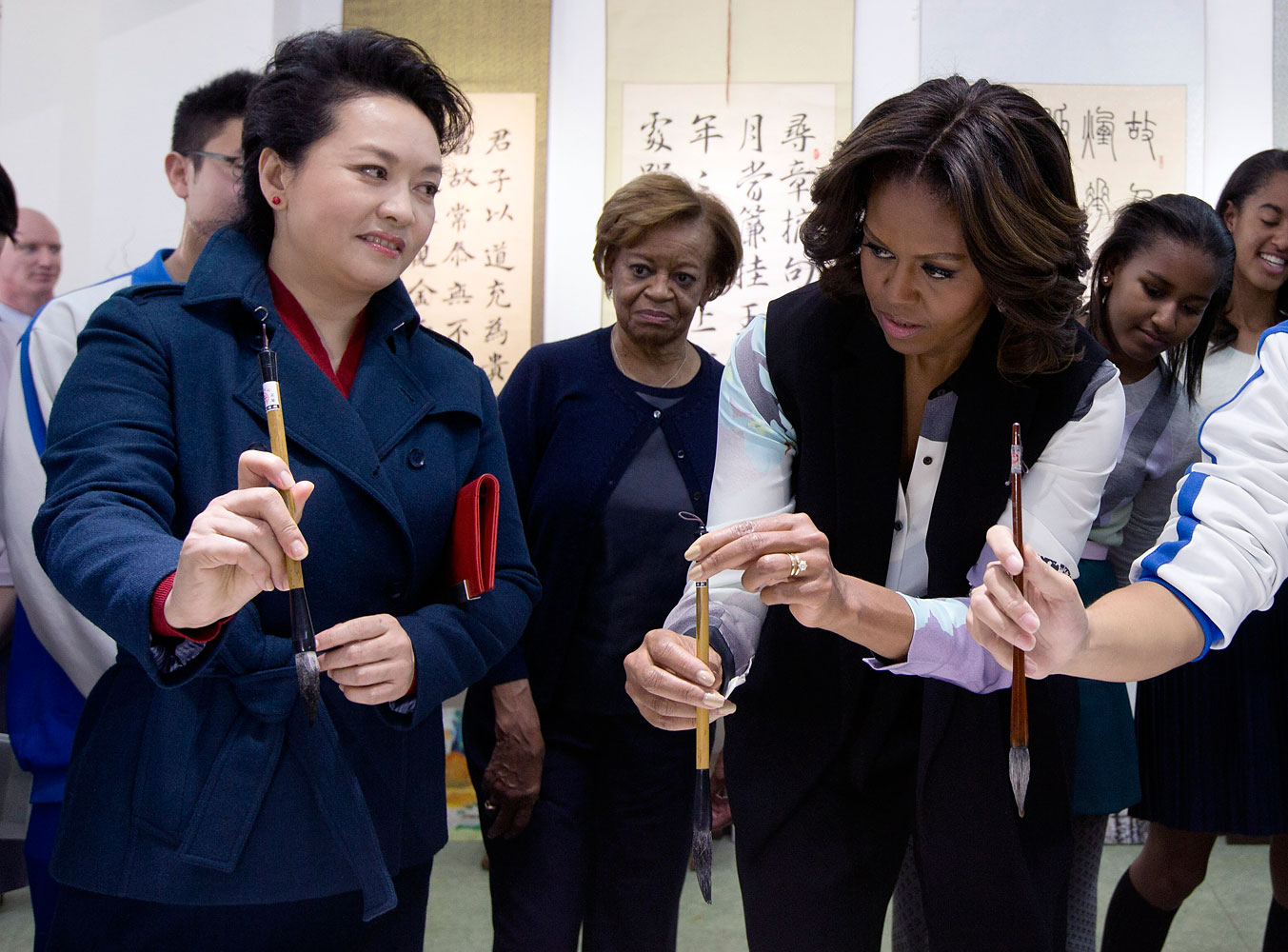 Peng Liyuan, wife of Chinese President Xi Jinping shows U.S. first lady Michelle Obama how to hold a writing brush as they visit a Chinese traditional calligraphy class at the Beijing Normal School, a school that prepares students to go abroad in Beijing