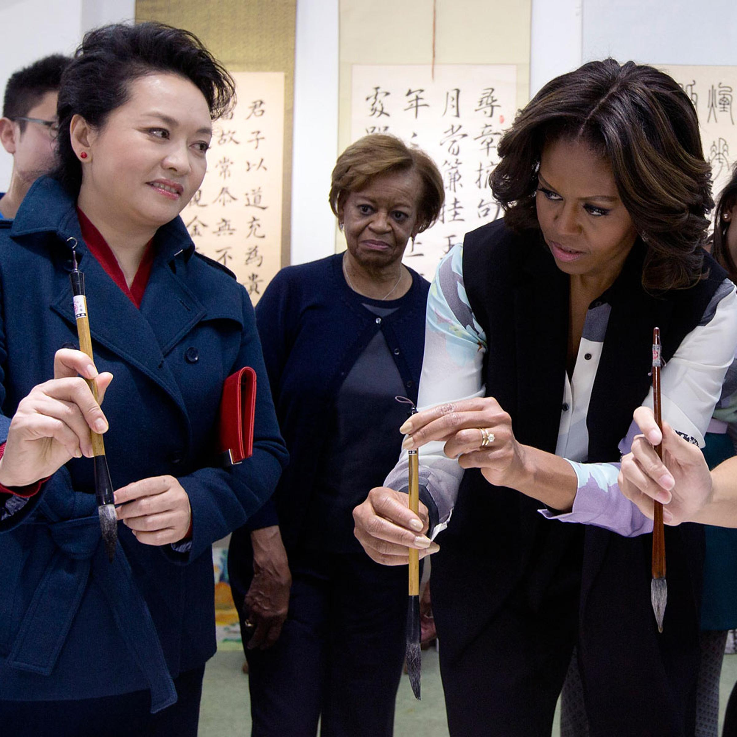 Peng Liyuan, wife of Chinese President Xi Jinping shows U.S. first lady Michelle Obama how to hold a writing brush as they visit a Chinese traditional calligraphy class at the Beijing Normal School, a school that prepares students to go abroad in Beijing