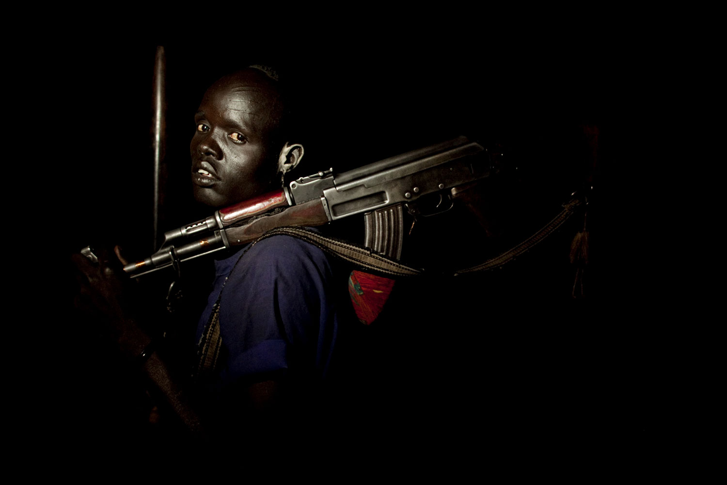 A young cattle keeper from the Dinka Rek sub-tribe poses for a portrait in a remote cattle camp in Wunlit County, southern Sudan. Young men like this man are often tasked with protecting cows from raids by neighboring communities. He holds an AK 47 assault rifle, a common weapon among young cattle keeping males. 