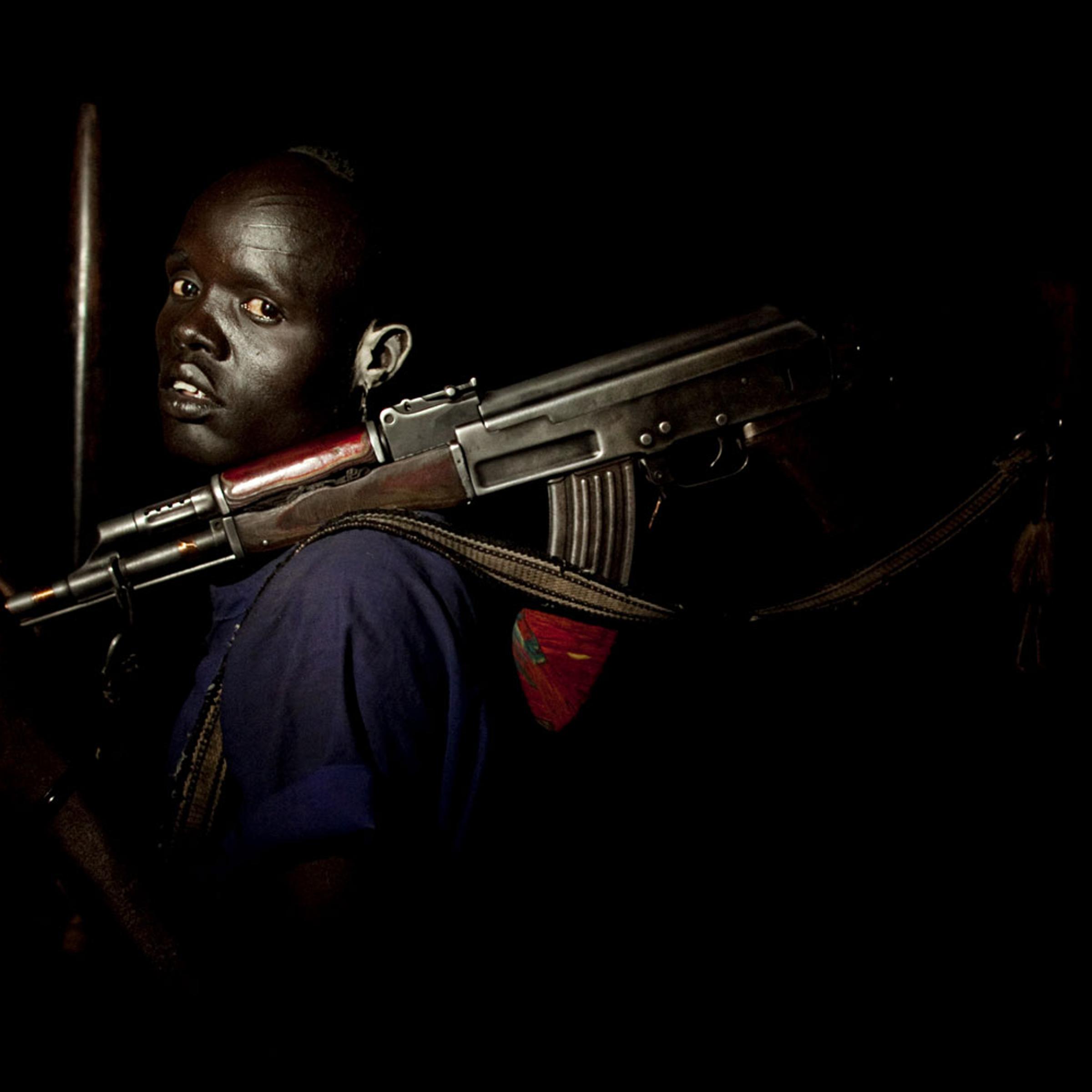 A young cattle keeper from the Dinka Rek sub-tribe poses for a portrait in a remote cattle camp in Wunlit County, southern Sudan. Young men like this man are often tasked with protecting cows from raids by neighboring communities. He holds an AK 47 assault rifle, a common weapon among young cattle keeping males.