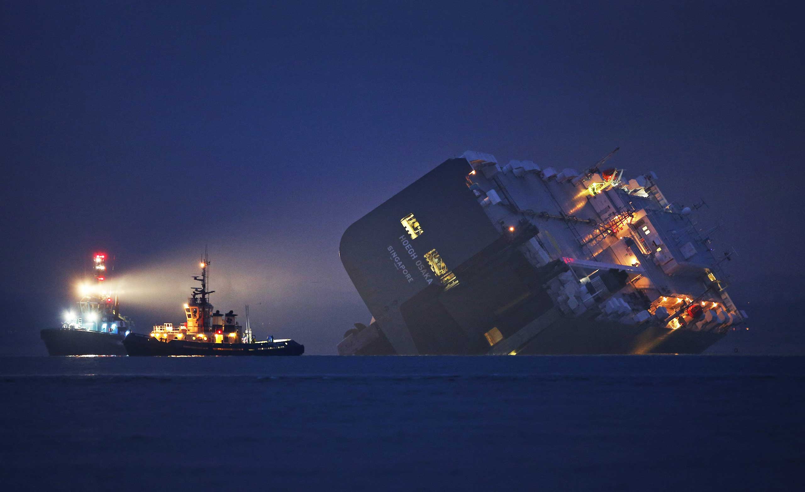 Jan 4. 2015. A salvage tug lights the hull of the stricken Hoegh Osaka cargo ship after it ran aground on a sand bank Cowes, England.