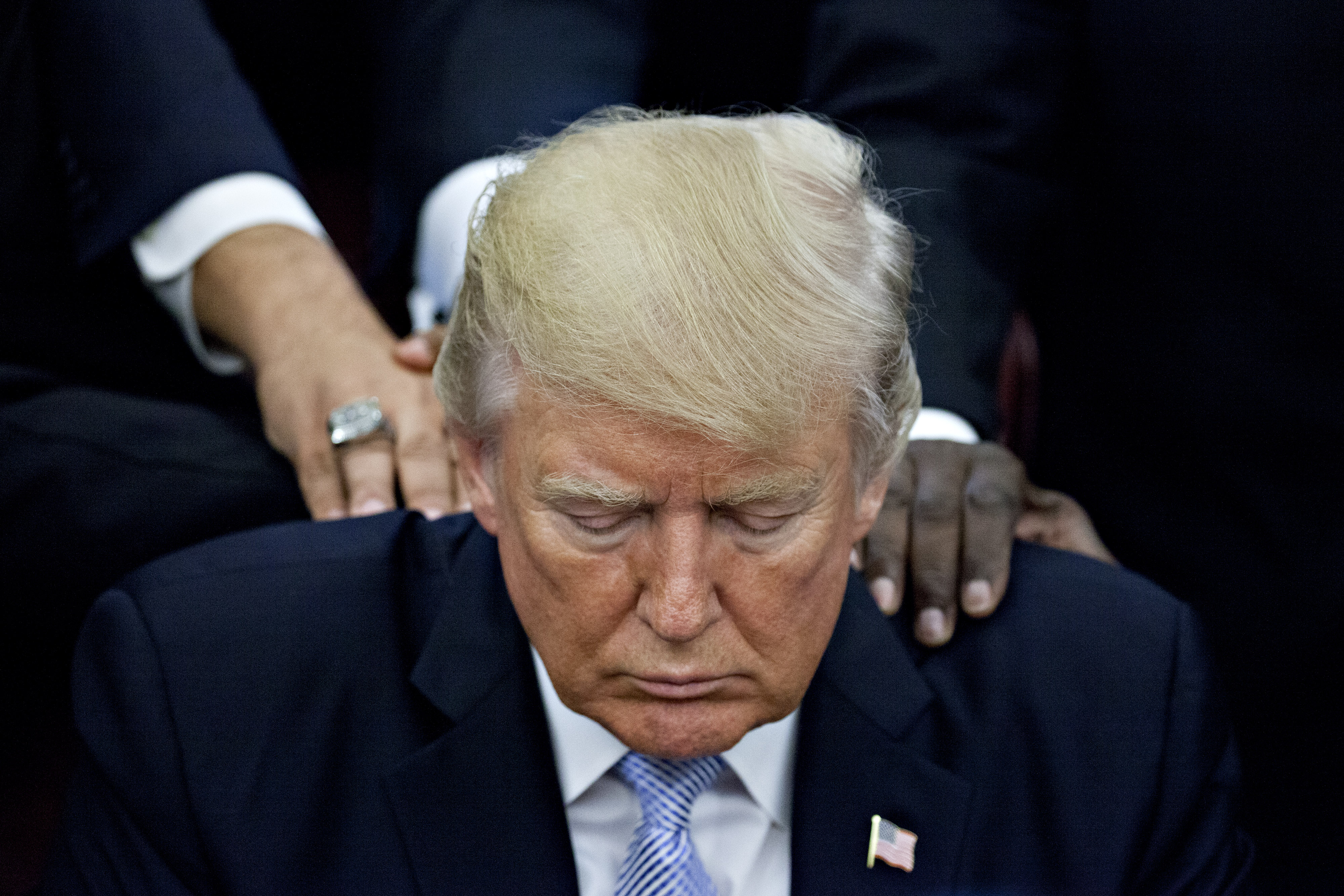 U.S. President Trump bows his head during a prayer while surrounded by faith leaders and evangelical ministers after signing a proclamation declaring a day of prayer in the Oval Office of the White House in Washington, D.C., U.S., on Friday, Sept. 1, 201