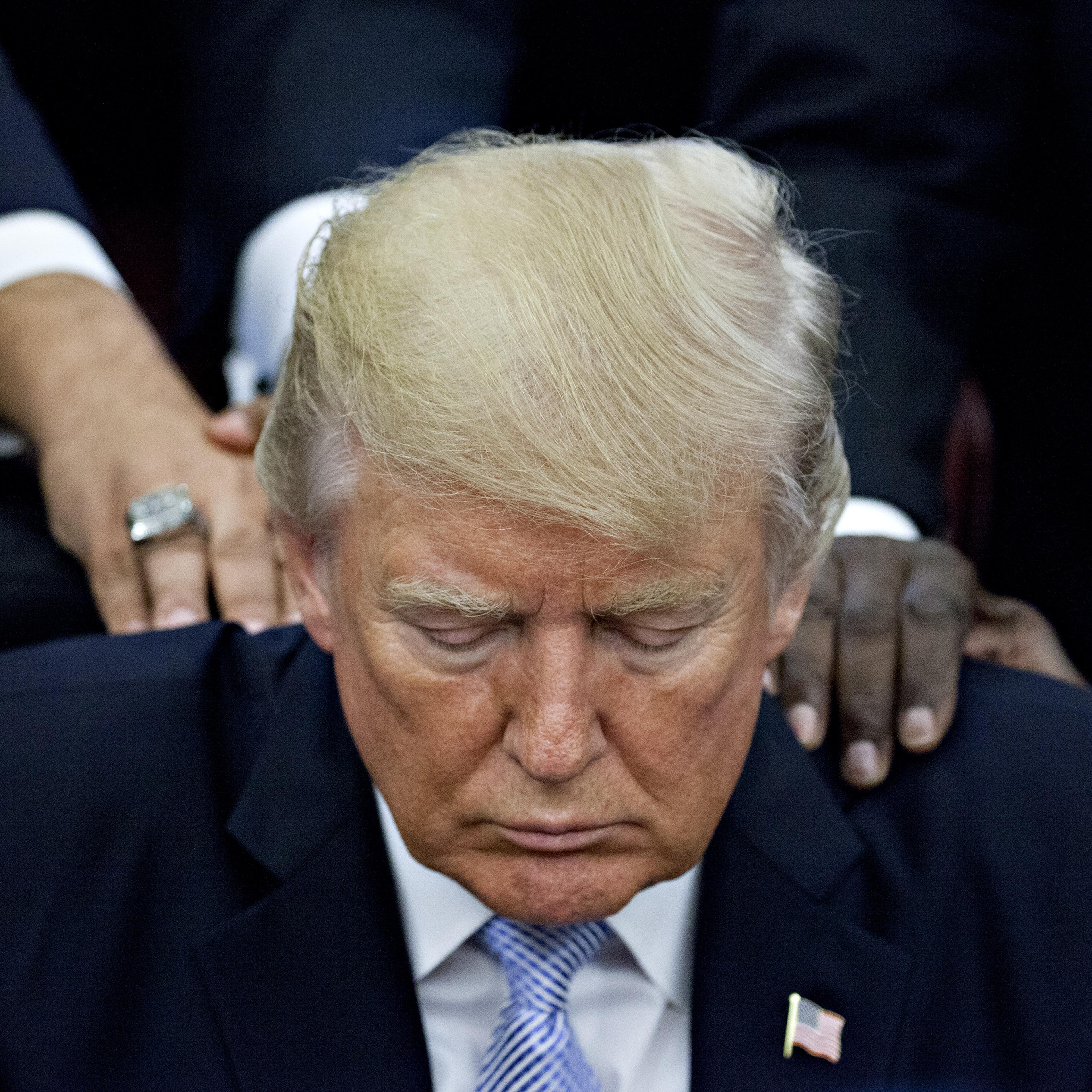 U.S. President Trump bows his head during a prayer while surrounded by faith leaders and evangelical ministers after signing a proclamation declaring a day of prayer in the Oval Office of the White House in Washington, D.C., U.S., on Friday, Sept. 1, 201