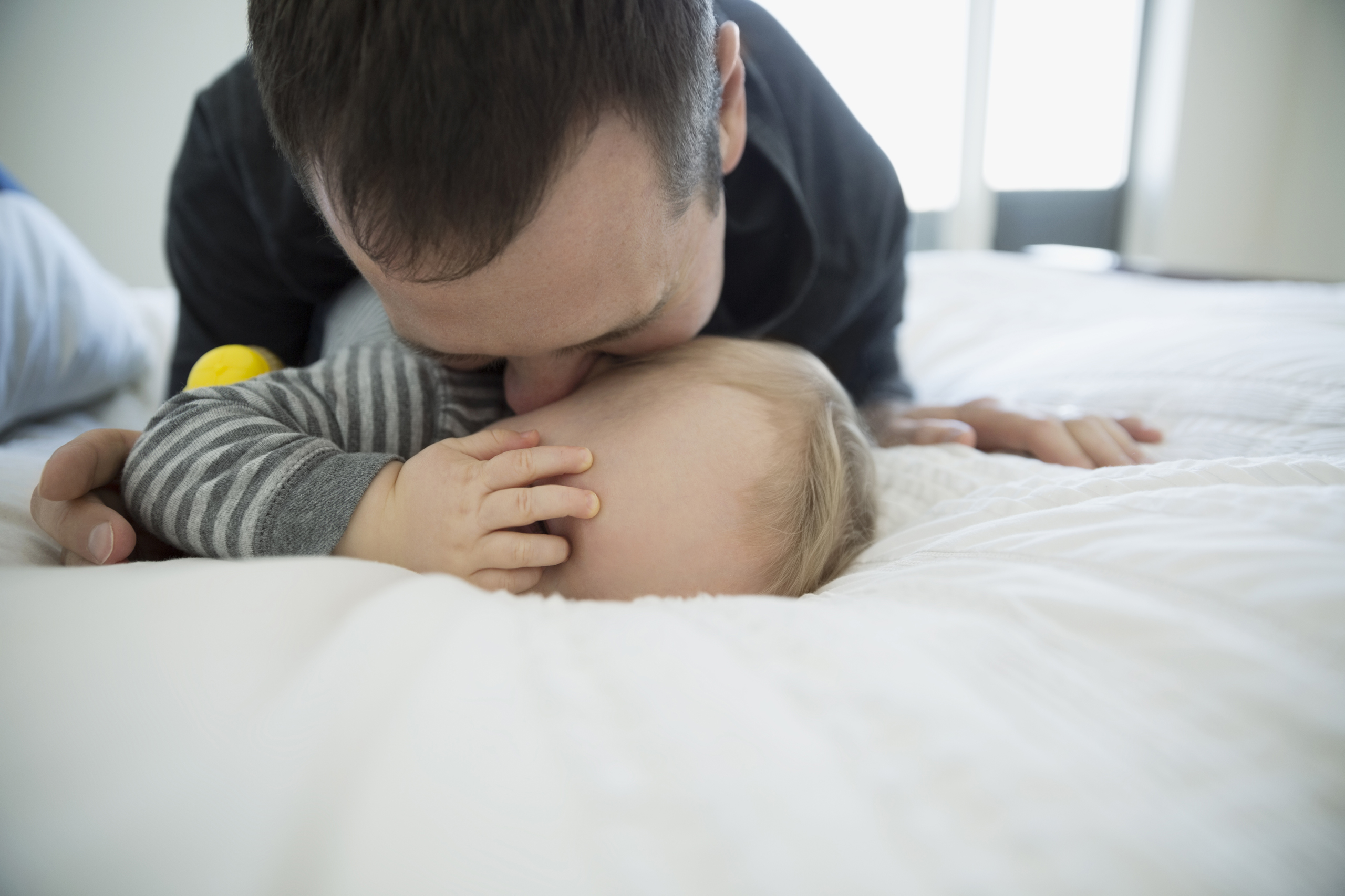Father kissing baby boy on bed