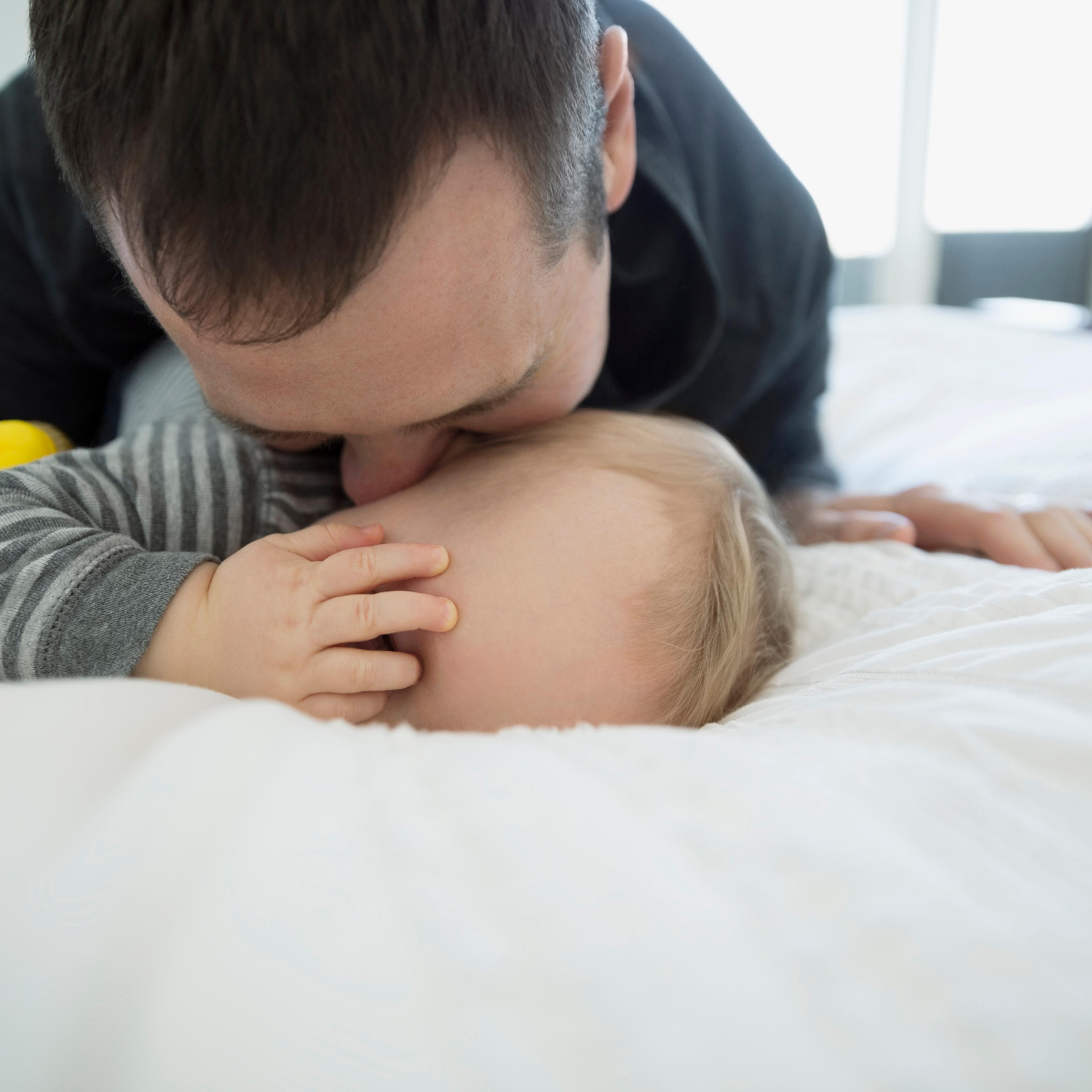 Father kissing baby boy on bed