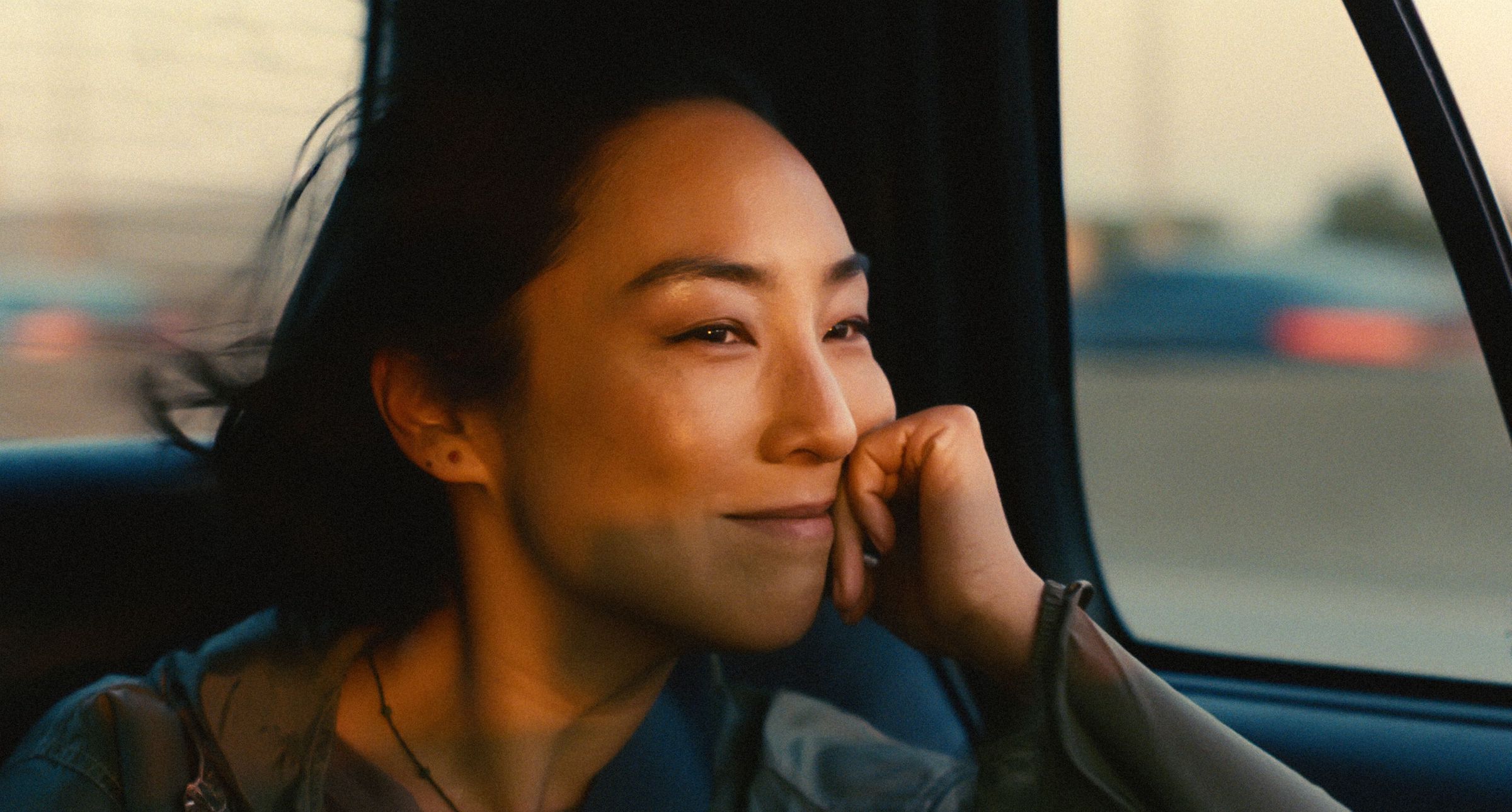 Nora (Greta Lee) smiles to herself as she drives in a taxi through New York City.