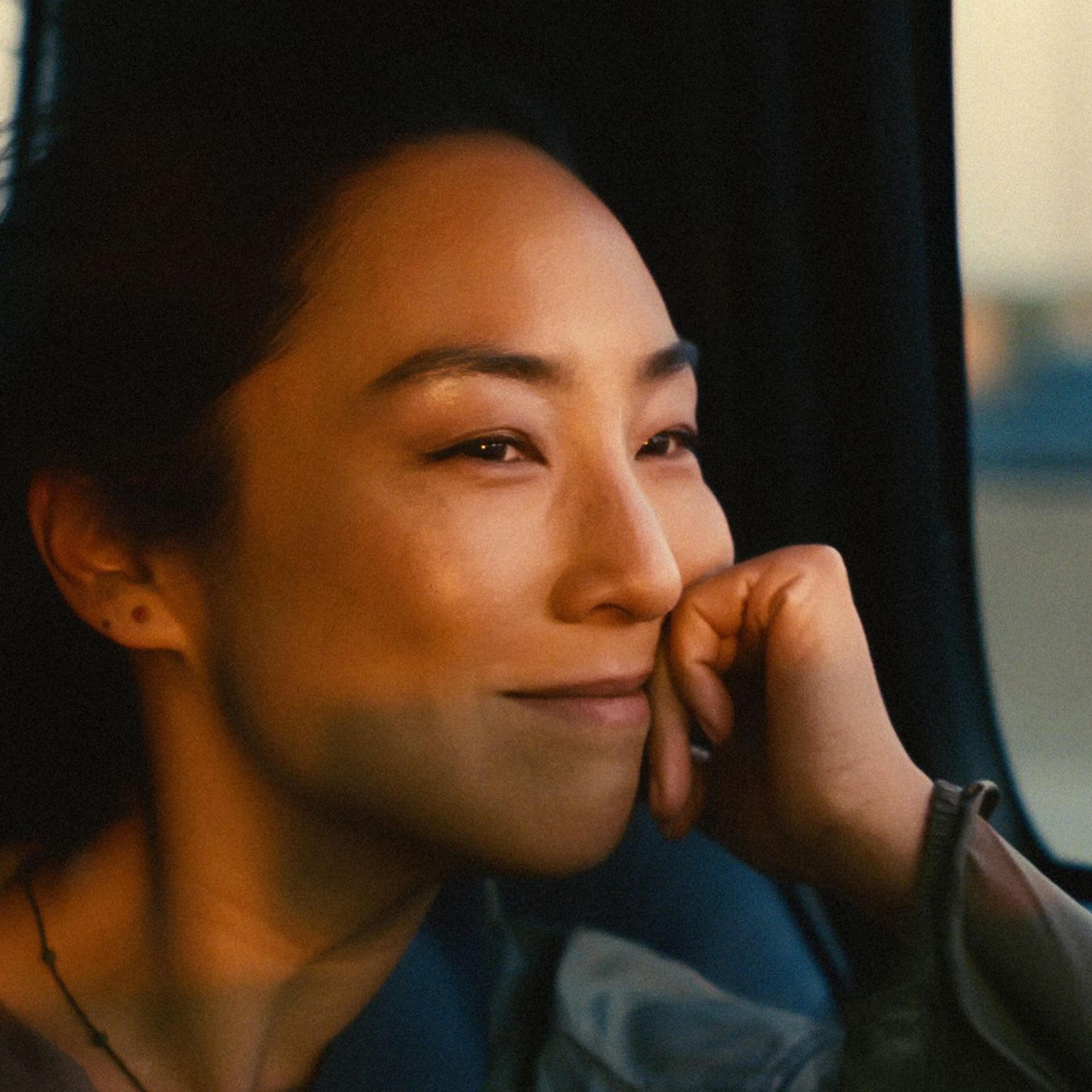 Nora (Greta Lee) smiles to herself as she drives in a taxi through New York City.