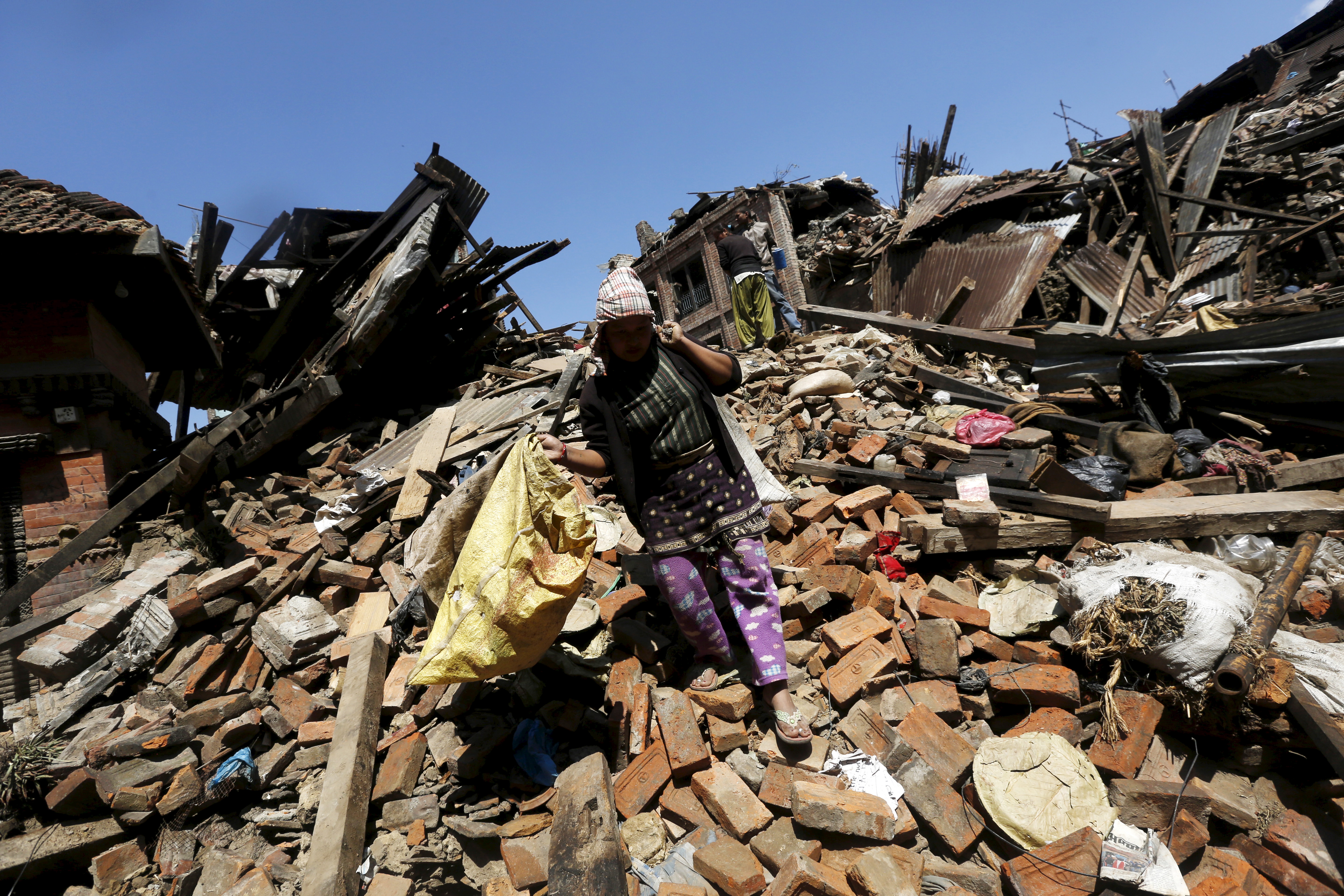 A woman carries belongings as she walks over collapsed house after earthquake in Bhaktapur