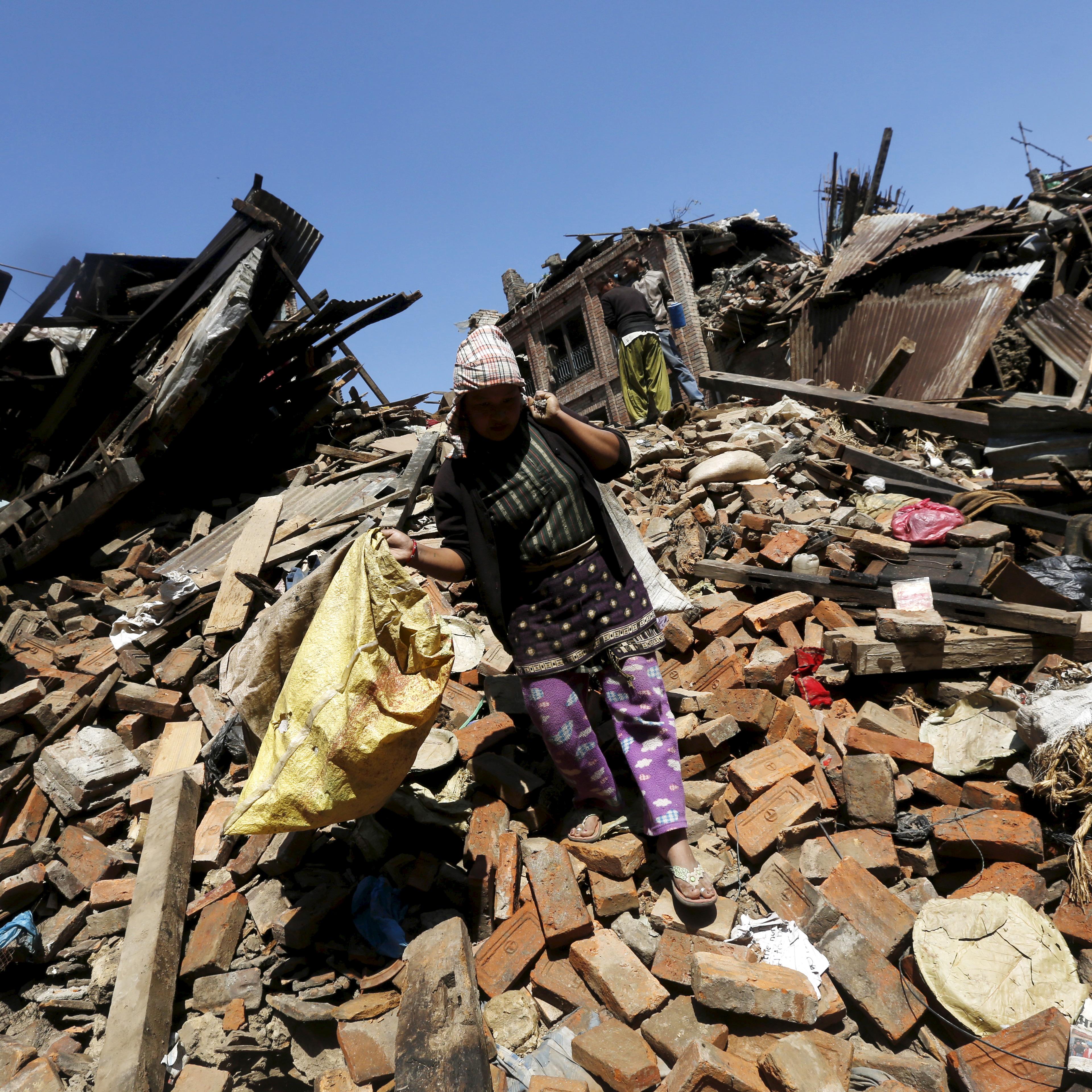 A woman carries belongings as she walks over collapsed house after earthquake in Bhaktapur