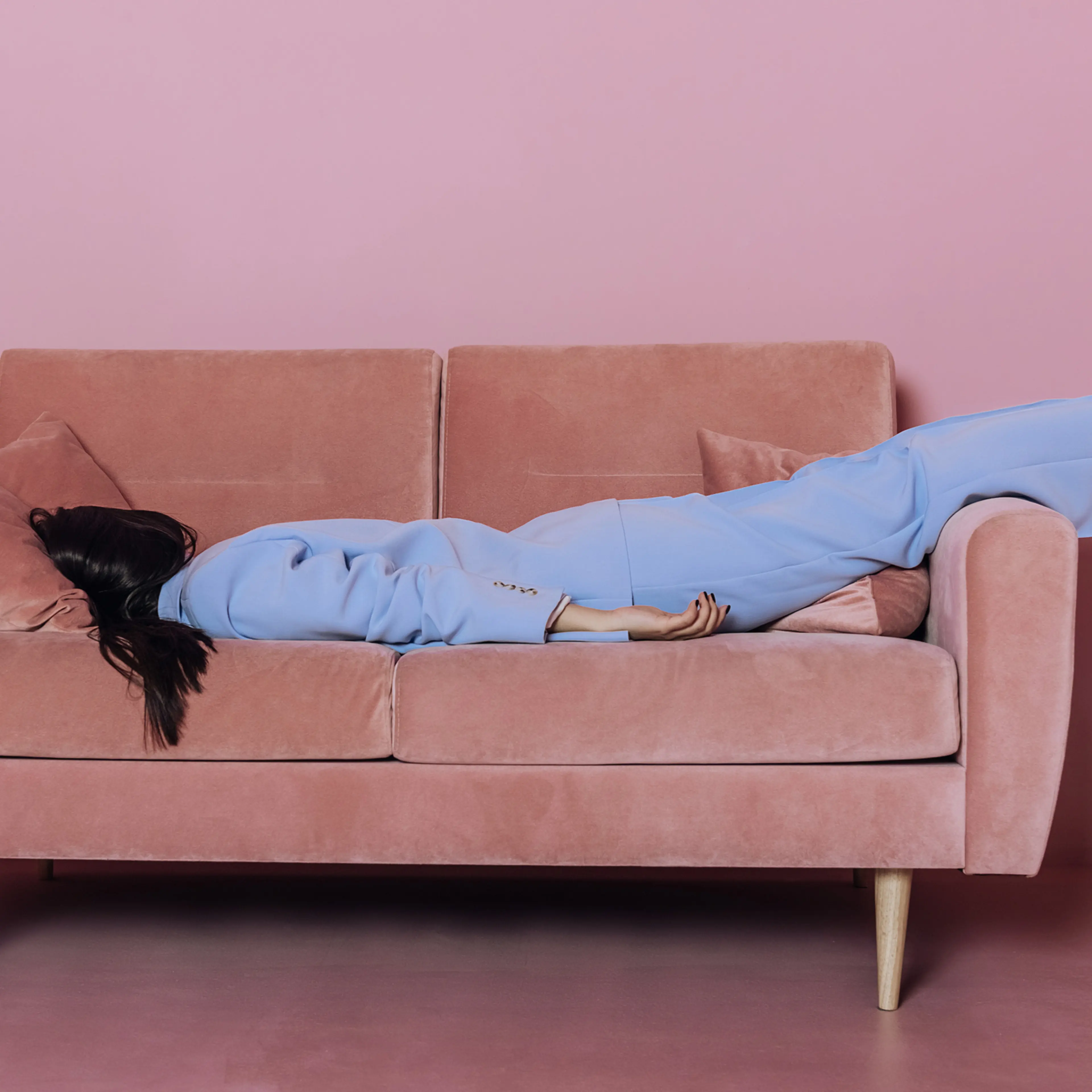 A woman lying in a blue suit on a pink sofa.