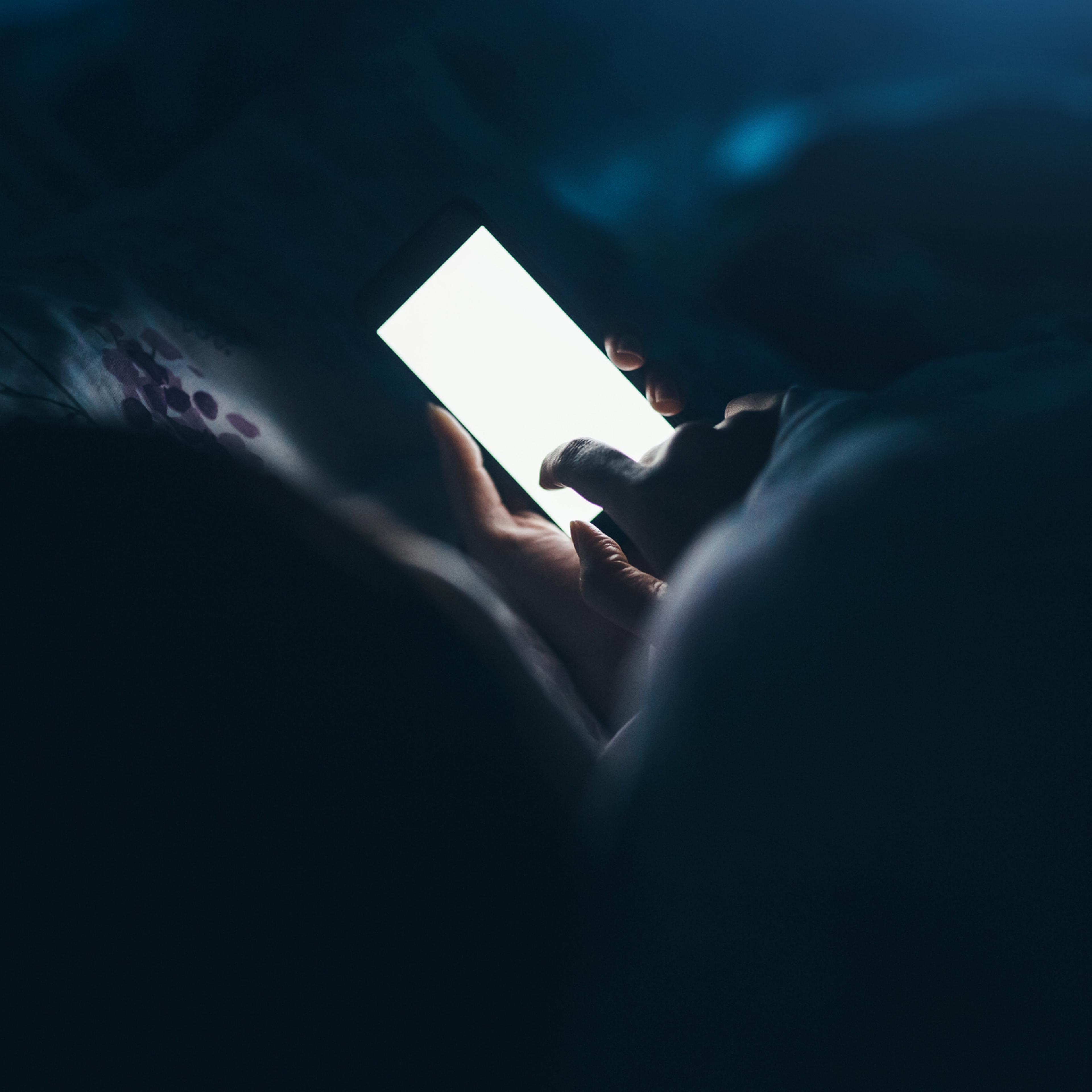 Woman texting and reading on smartphone in bed
