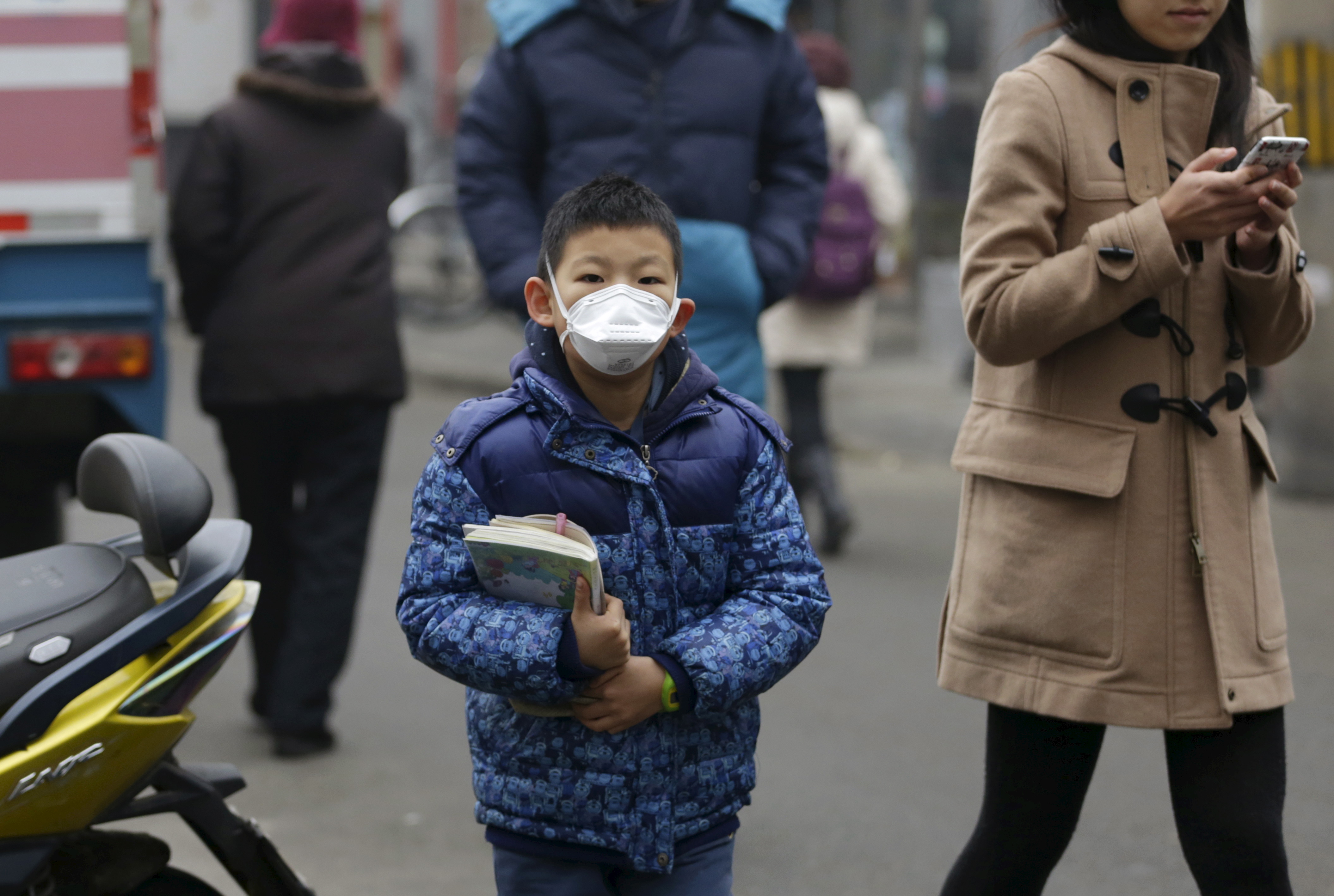A primary school student wearing a mask walks along a street with his textbooks amid heavy smog after his school was closed due to the first ever "red alert" for air pollution, in central Beijing