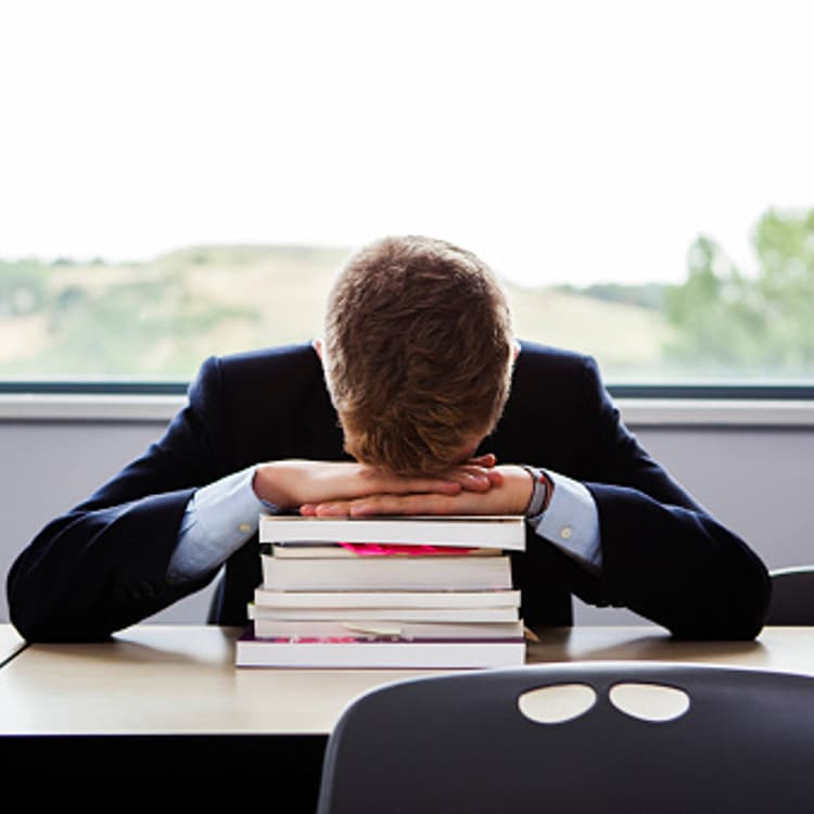 male-student-sitting-books-head-down