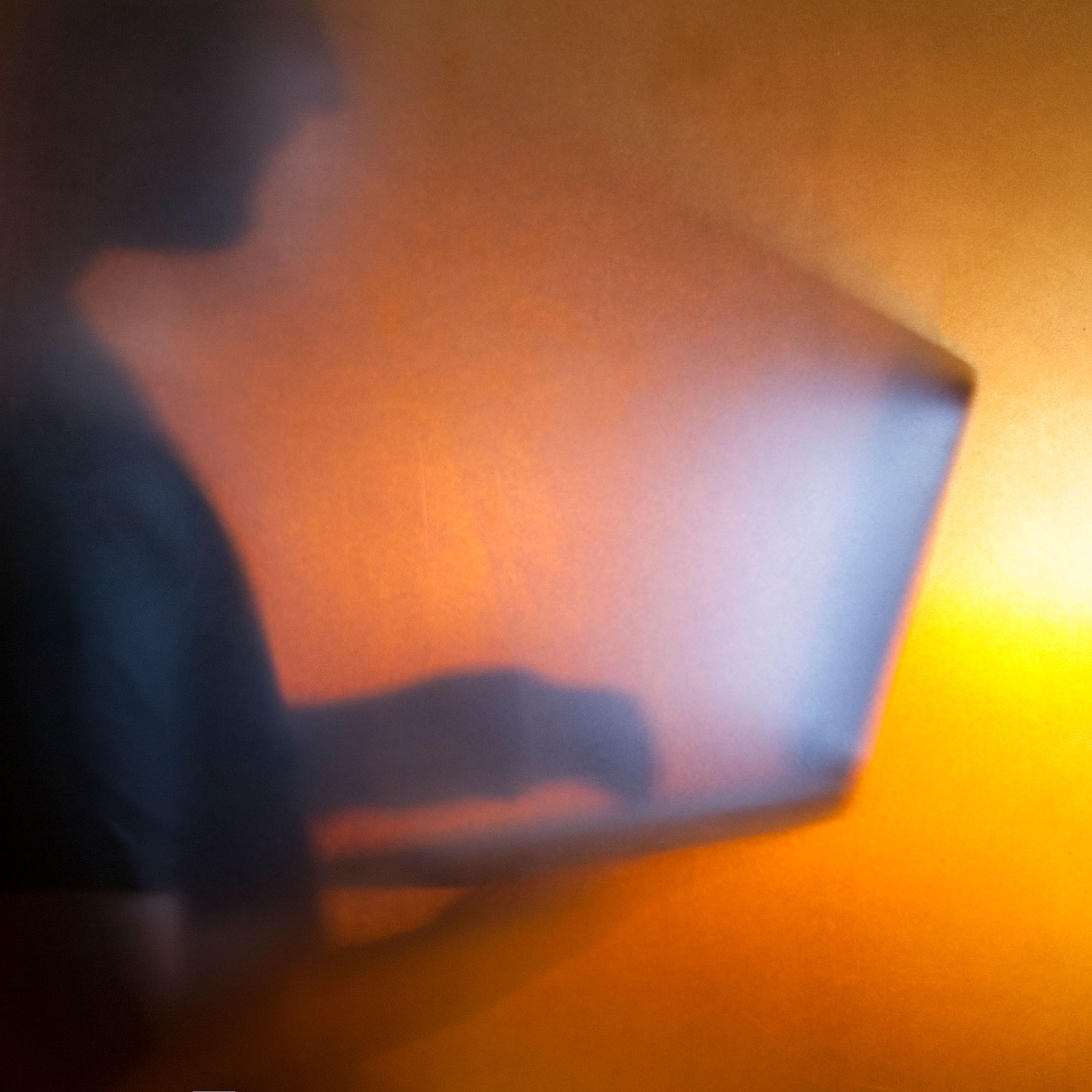 Man using laptop behind translucent glass with warm background