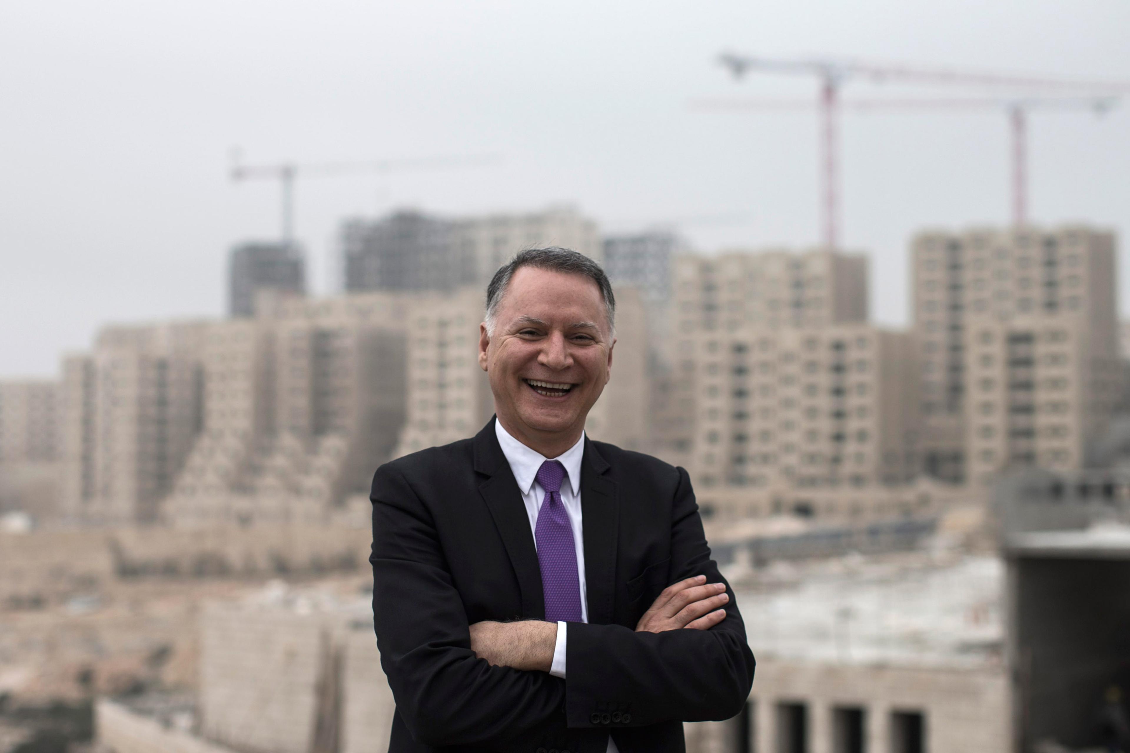 epa04099136 Bashar Masri, main investor of the new Palestinian city of Rawabi, poses for a portrait picture backdropped by apartment building under construction in Rawabi, West Bank, 24 February 2014. Rawabi is the first Palestinian planned city located