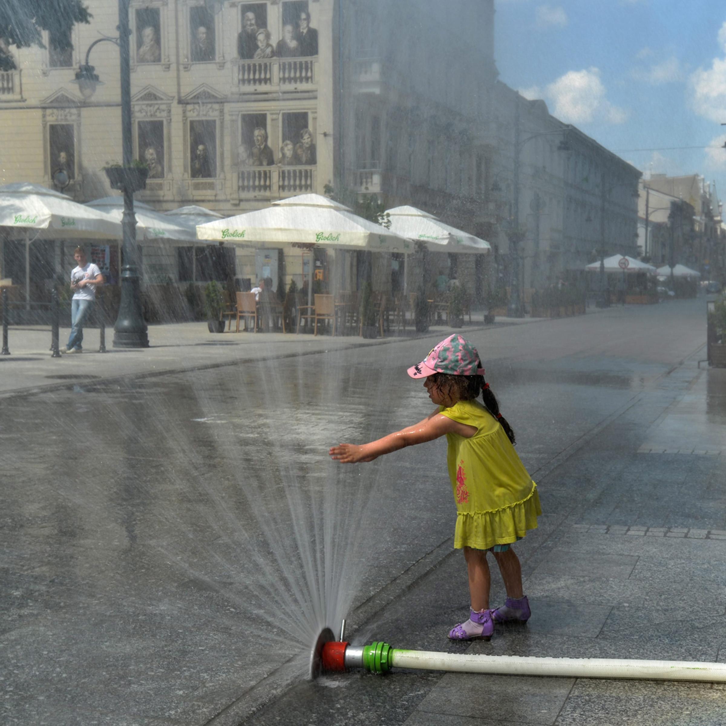 A girl plays with the water curtains that have been installed by firemen to bring relief to local people suffering from scorching heat on Piotrowska Street in Lodz, Poland on May 24, 2014.