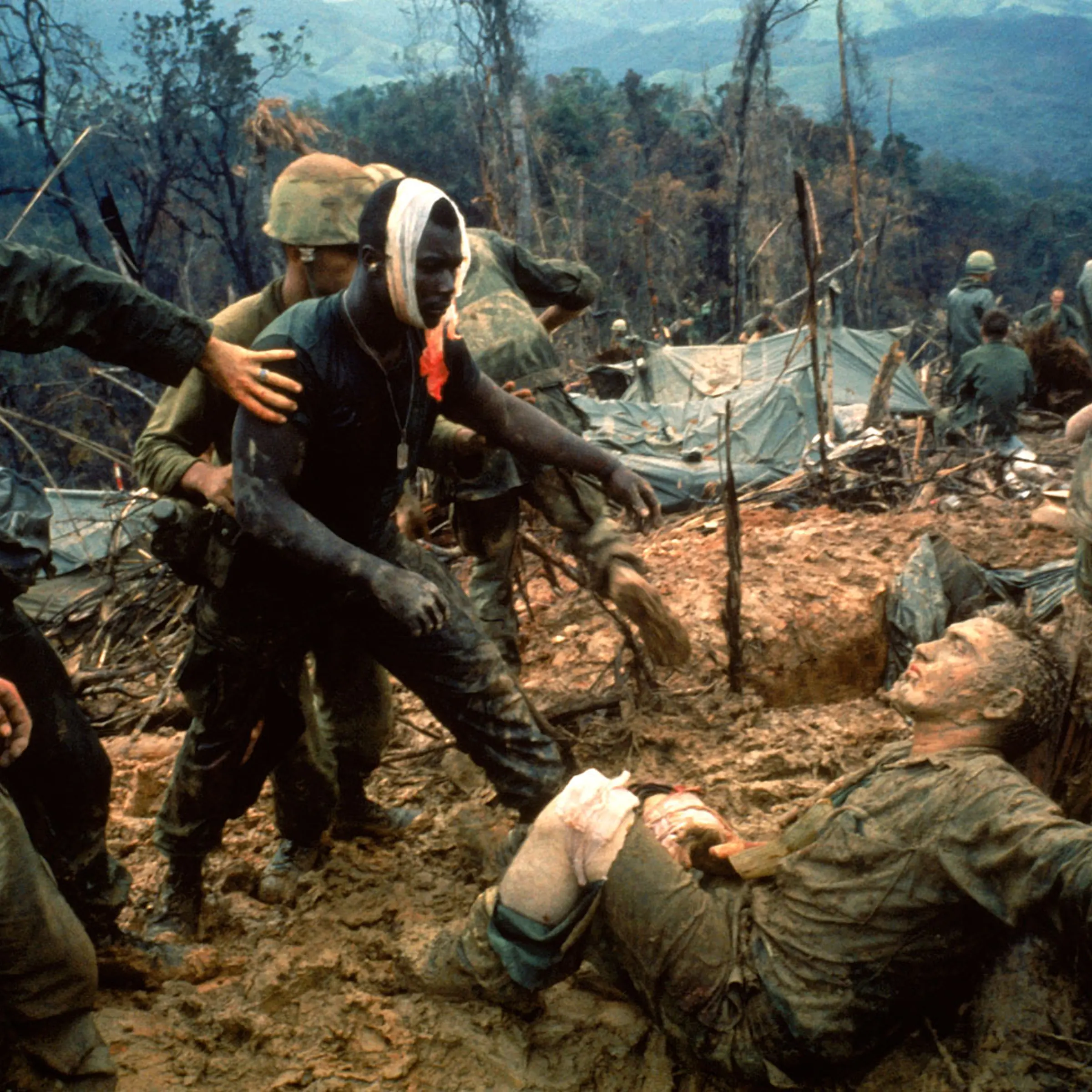 Wounded Marine Gunnery Sgt. Jeremiah Purdie (center, with bandaged head) reaches toward a stricken comrade after a fierce firefight south of the DMZ, Vietnam, October 1966.