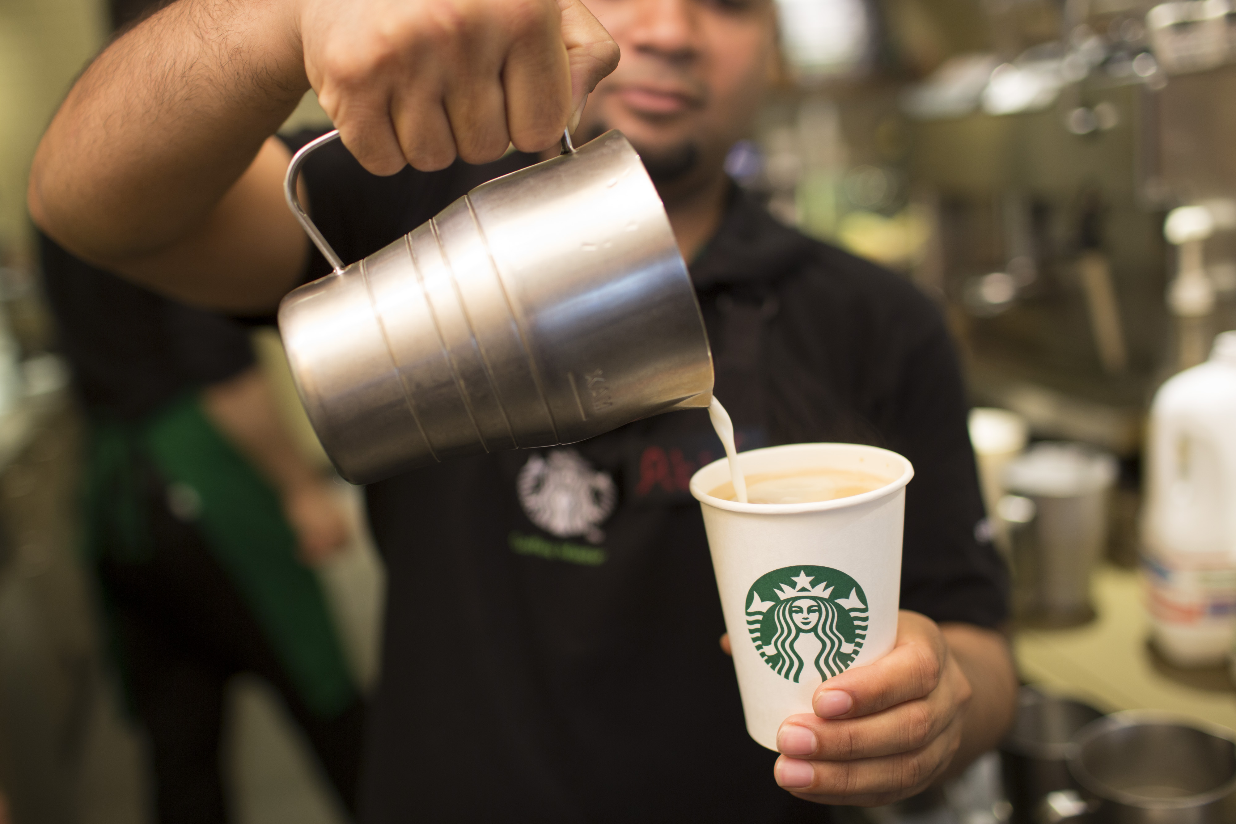 An employee pours milk into a cardboard coffee cup inside a Starbucks Corp. coffee shop in London on June 9, 2014.