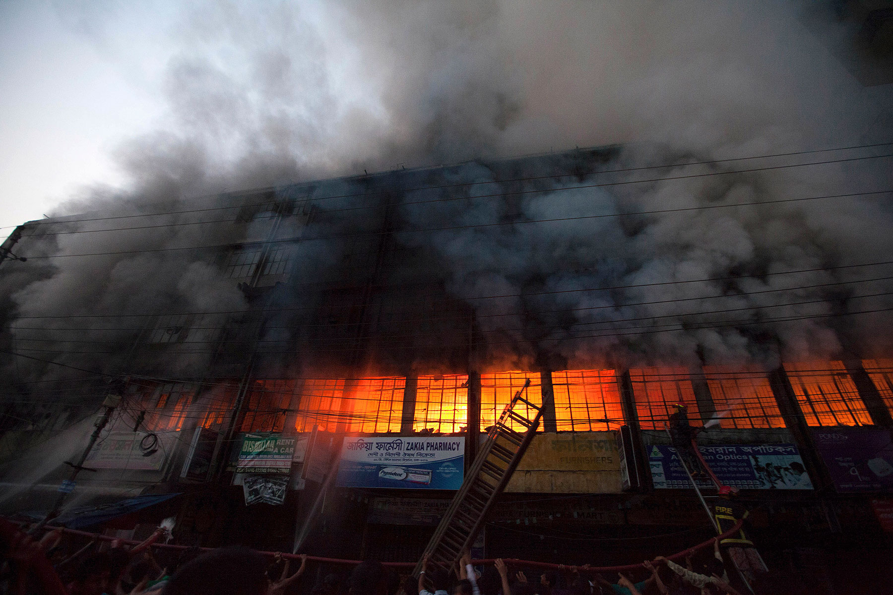 Locals and fire-fighters try to control a fire at a garment factory in Dhaka March 6, 2014