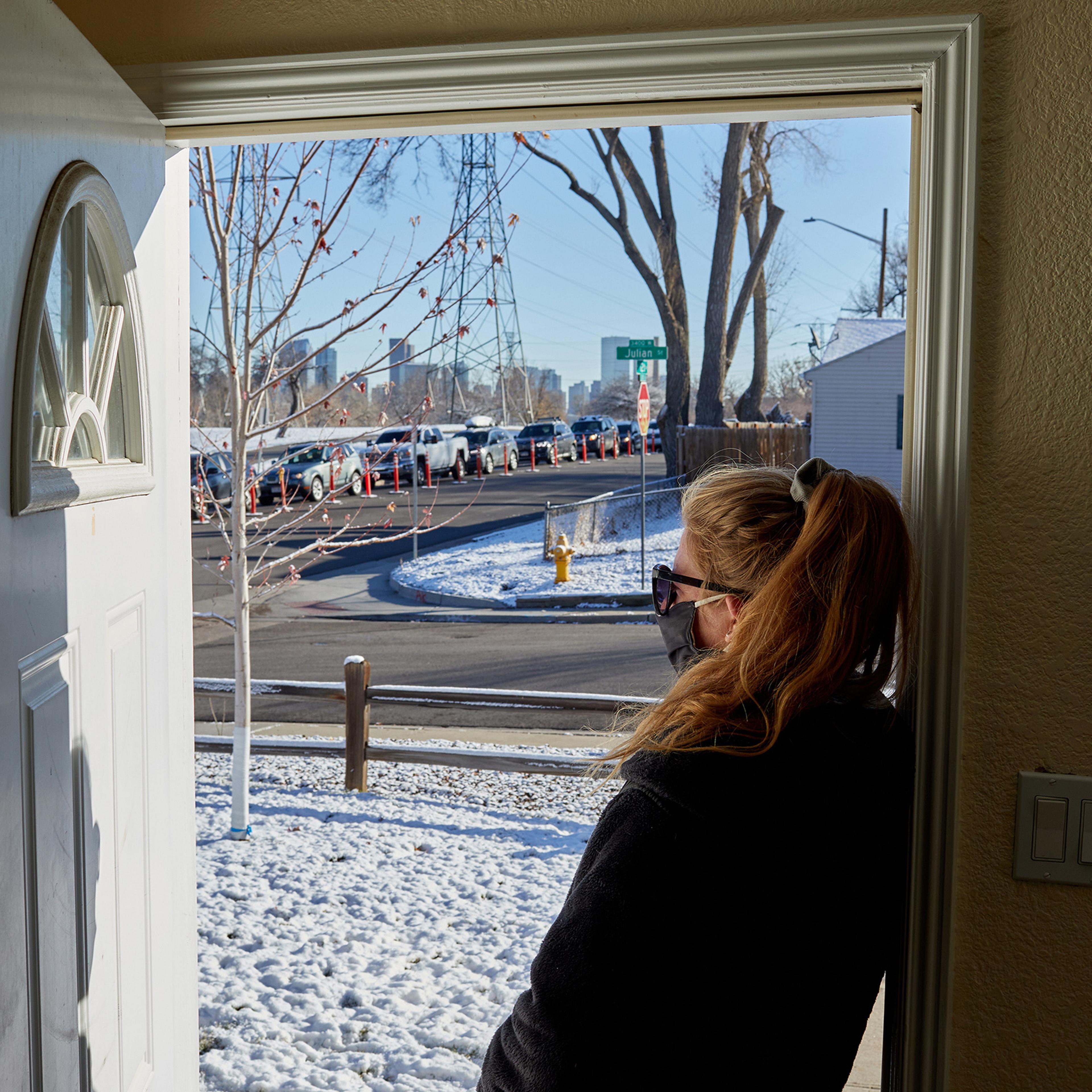 A Denver woman looks out from her home, on Nov. 10., at a line of cars with people waiting to get tested for COVID-19