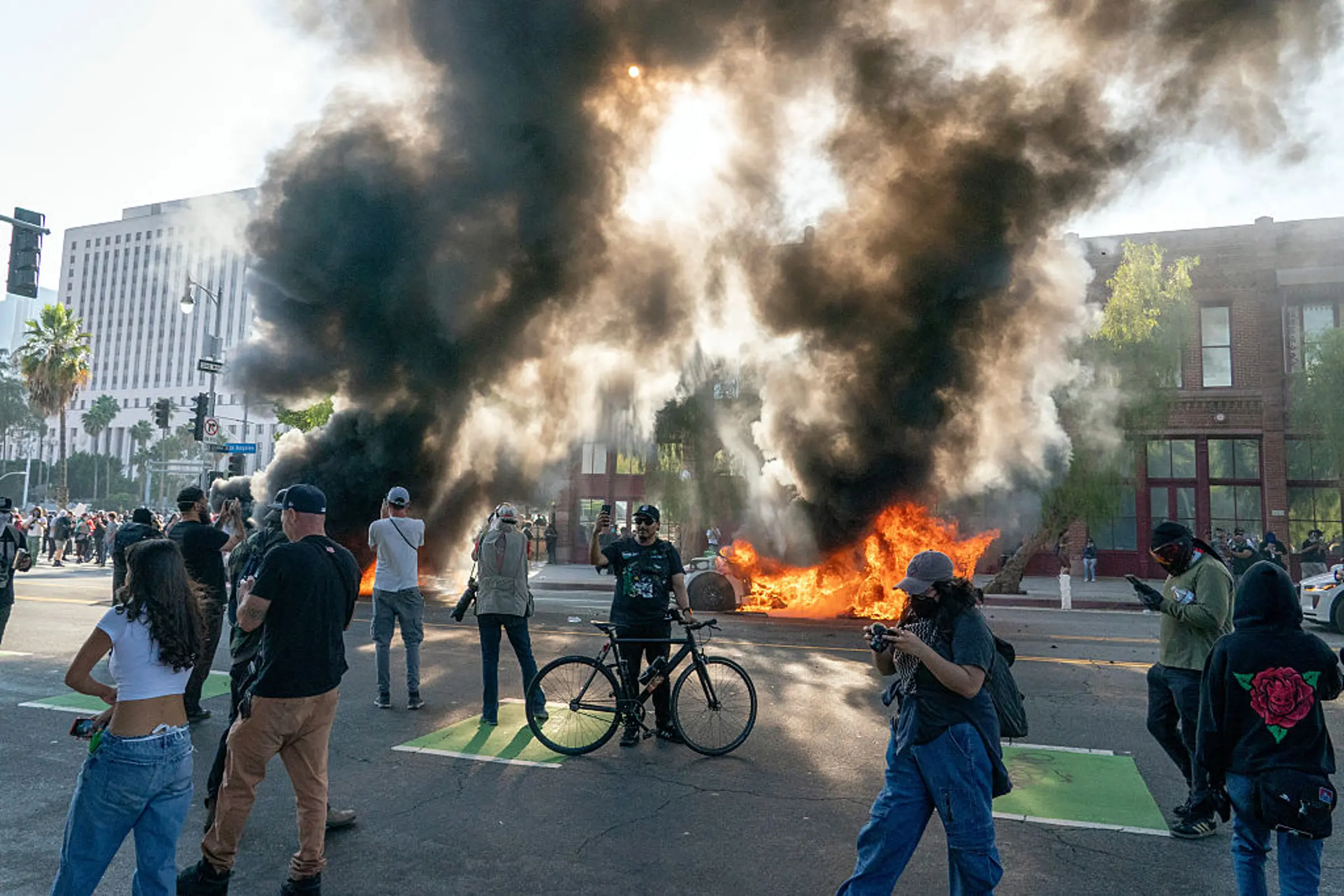 Cars burn behind protesters during a demonstration in Los Angeles, California, US, on June 8, 2025.