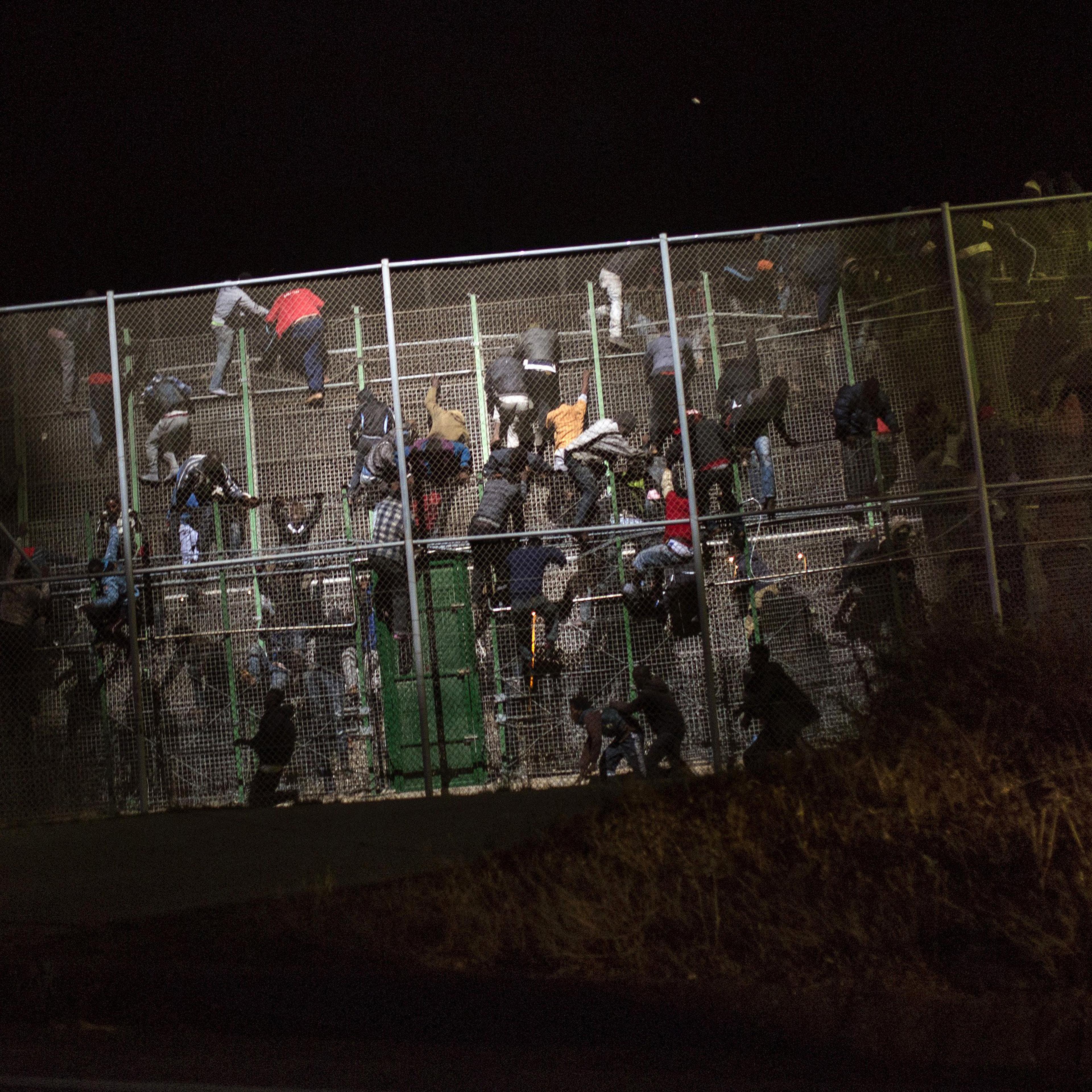 Sub-Saharan migrants scale a metallic fence that divides Morocco and the Spanish enclave of Melilla, early on May 28, 2014.
