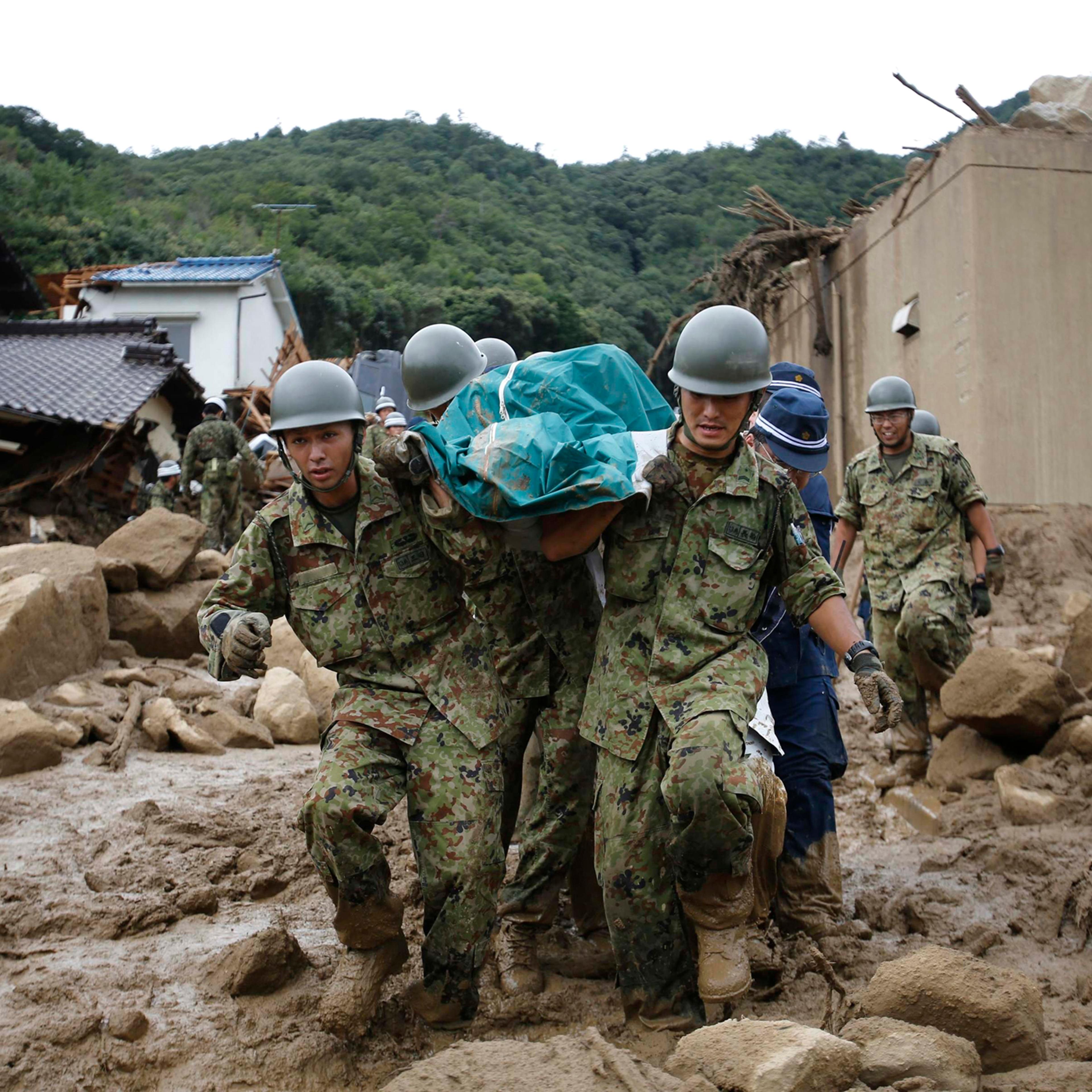 Japan Self-Defense Force soldiers and police officers carry the body of a victim in a plastic bag at a site where a landslide swept through a residential area at Asaminami ward in Hiroshima, western Japan, Aug. 20, 2014.