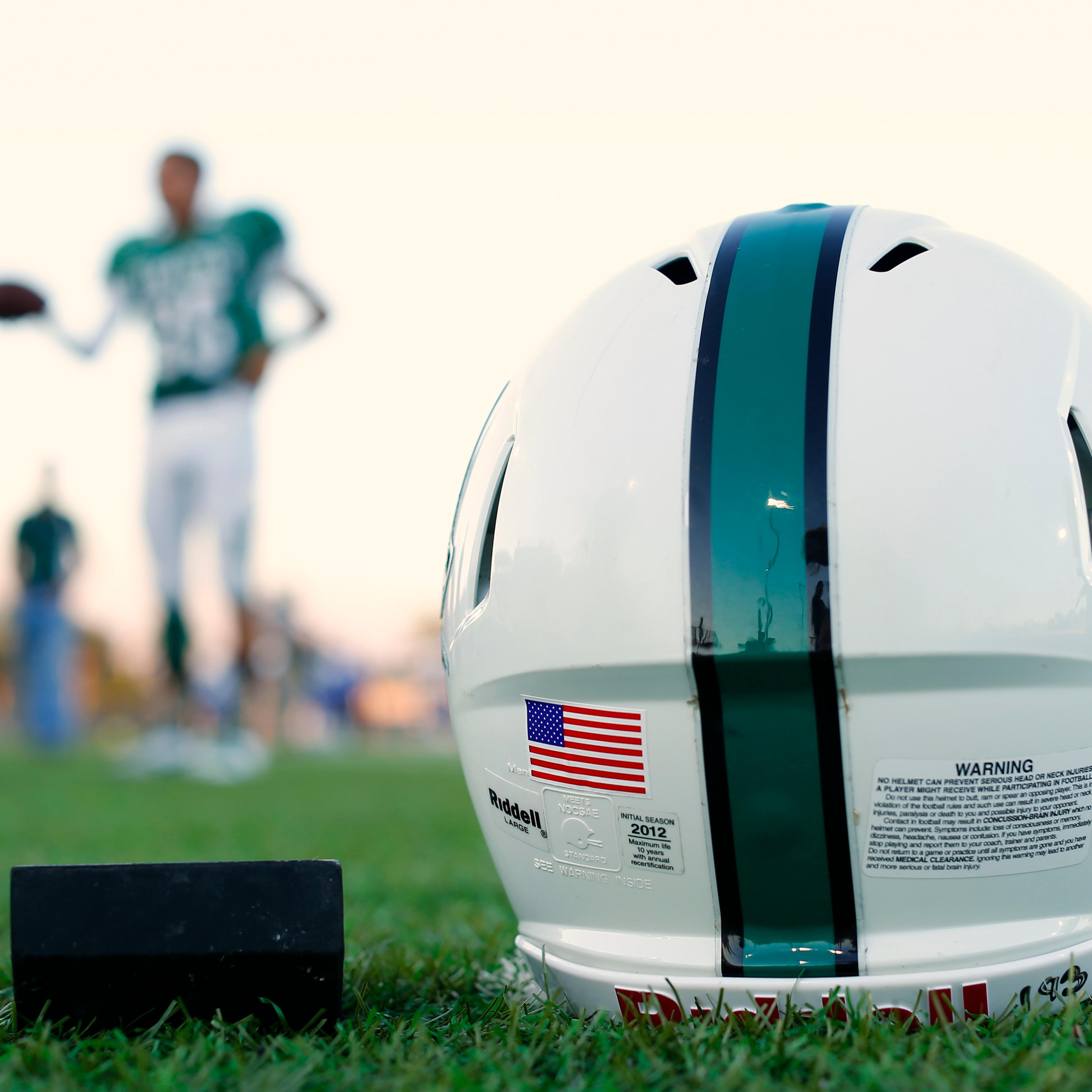 A football helmet's health warning sticker is pictured between a U.S. flag and the number 55, in memory of former student and NFL player Junior Seau, as the Oceanside Pirates high school football team prepares for their Friday night game in Oceanside
