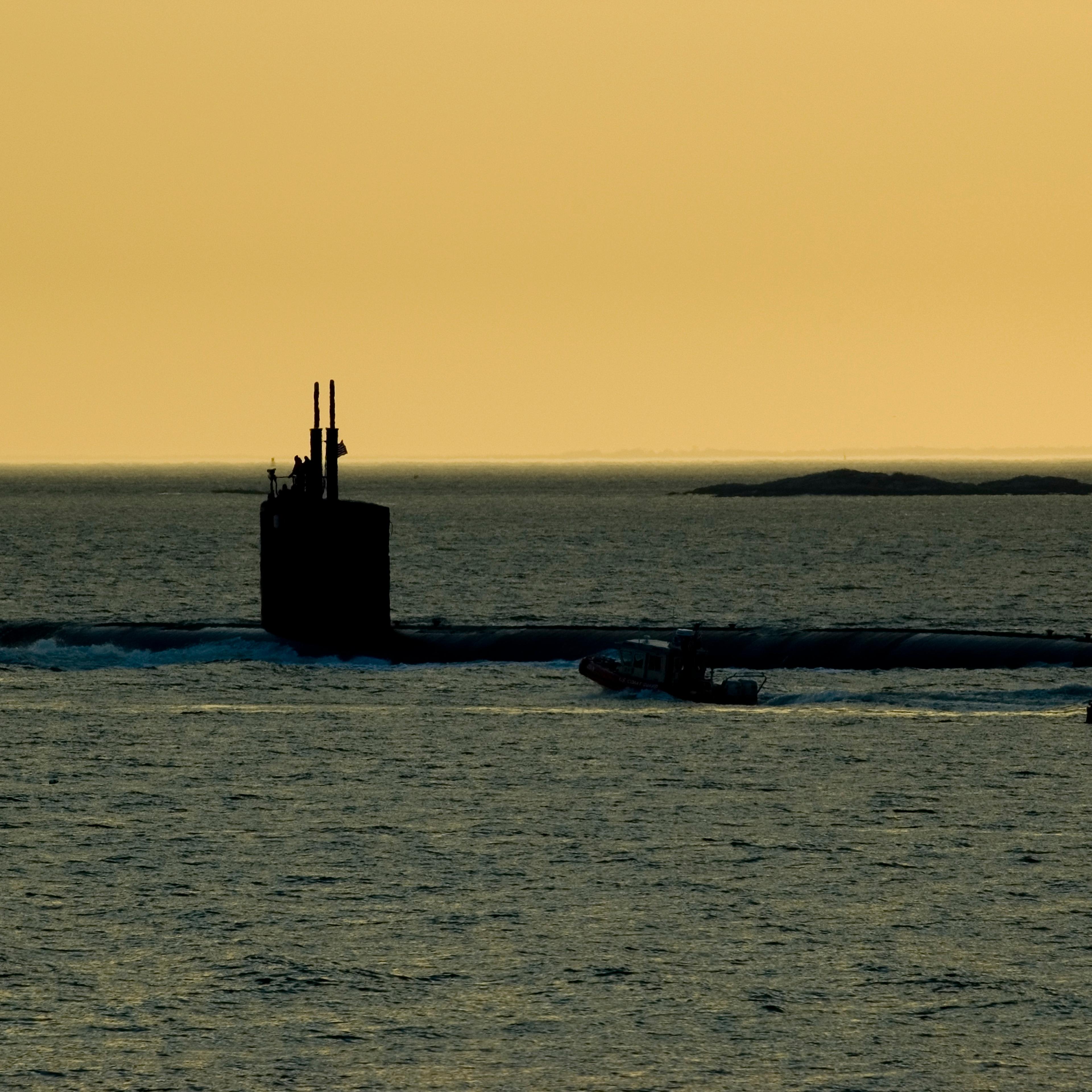 Silhouette of a submarine being followed by a coast guard zodiac.