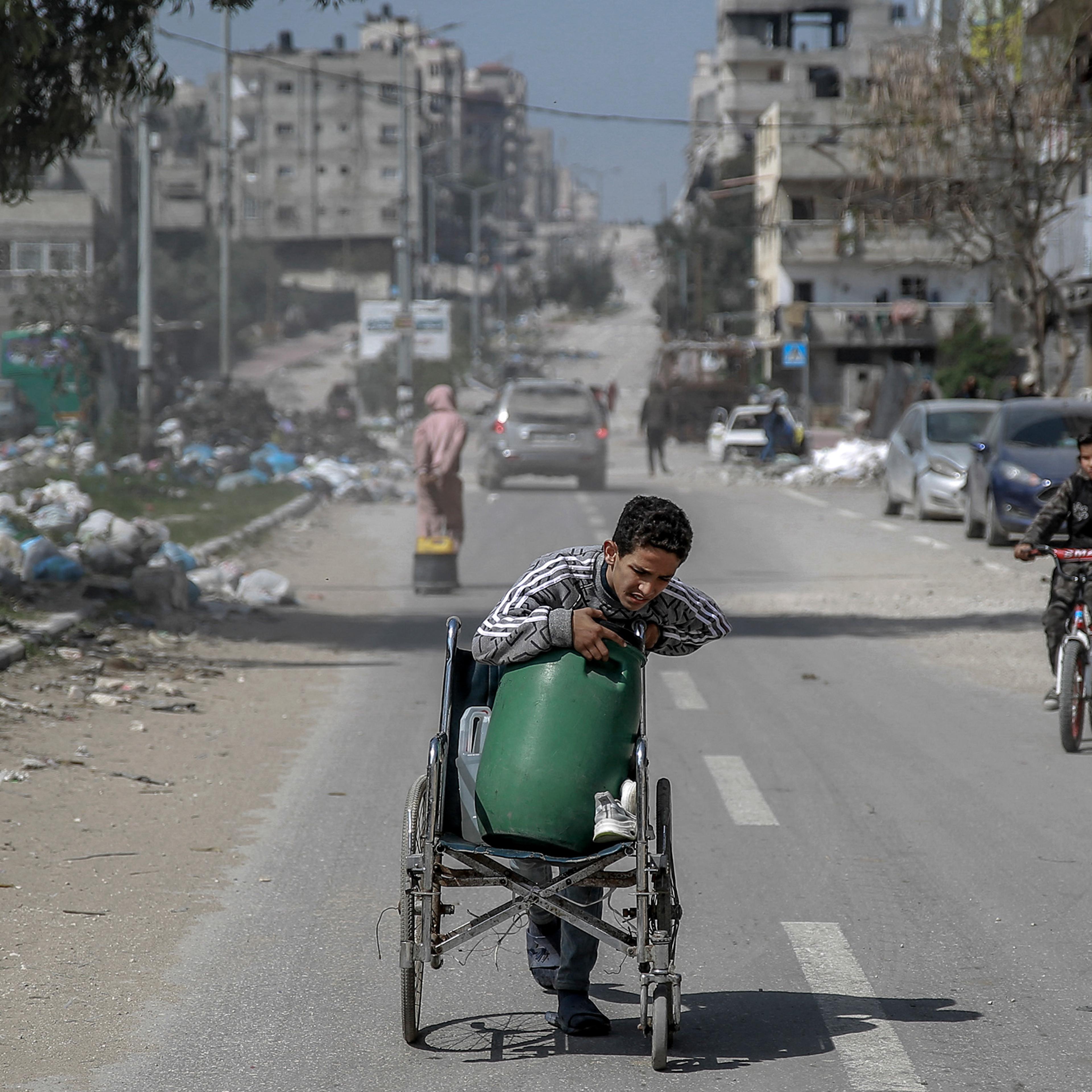 A Palestinian boy transports a water container on a wheelchair along a street in Gaza City on March 3, amid the ongoing conflict between Israel and Hamas.
