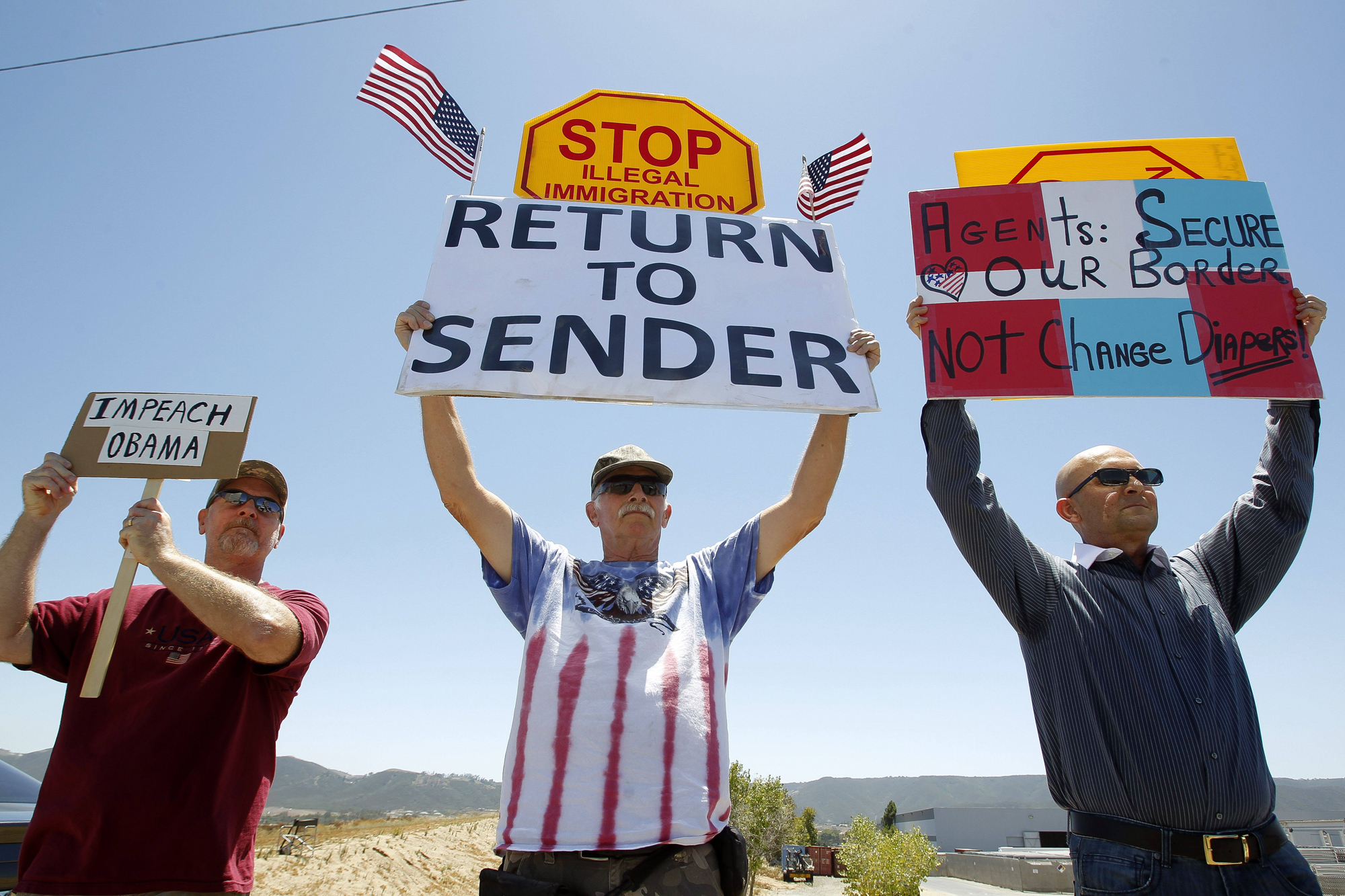 Protesters hold signs as they and other protesters wait for three buses containing undocumented immigrant women and children to arrive at the Border Patrol facility in Murrieta on July 1, in Murrieta, Calif.