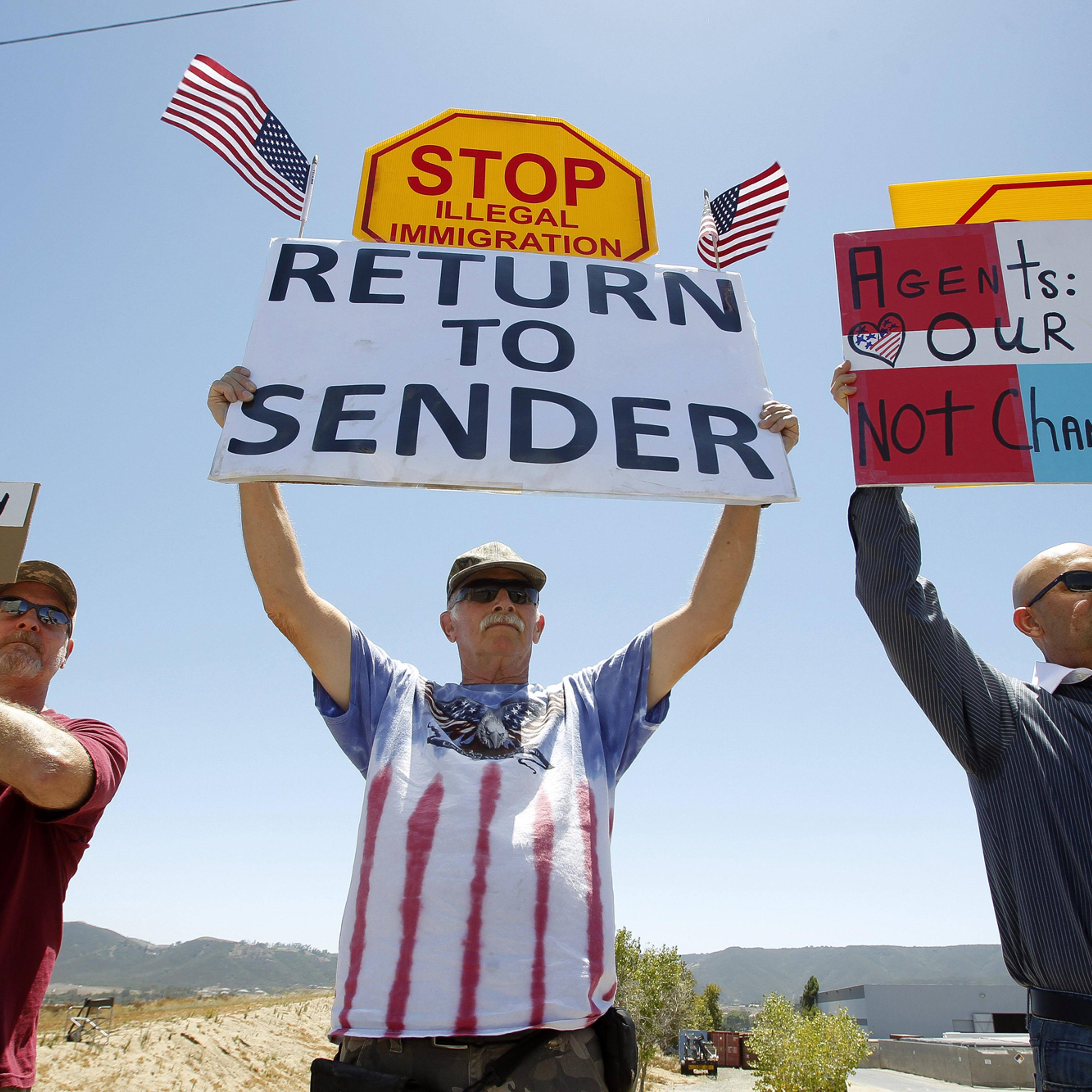 Protesters hold signs as they and other protesters wait for three buses containing undocumented immigrant women and children to arrive at the Border Patrol facility in Murrieta on July 1, in Murrieta, Calif.