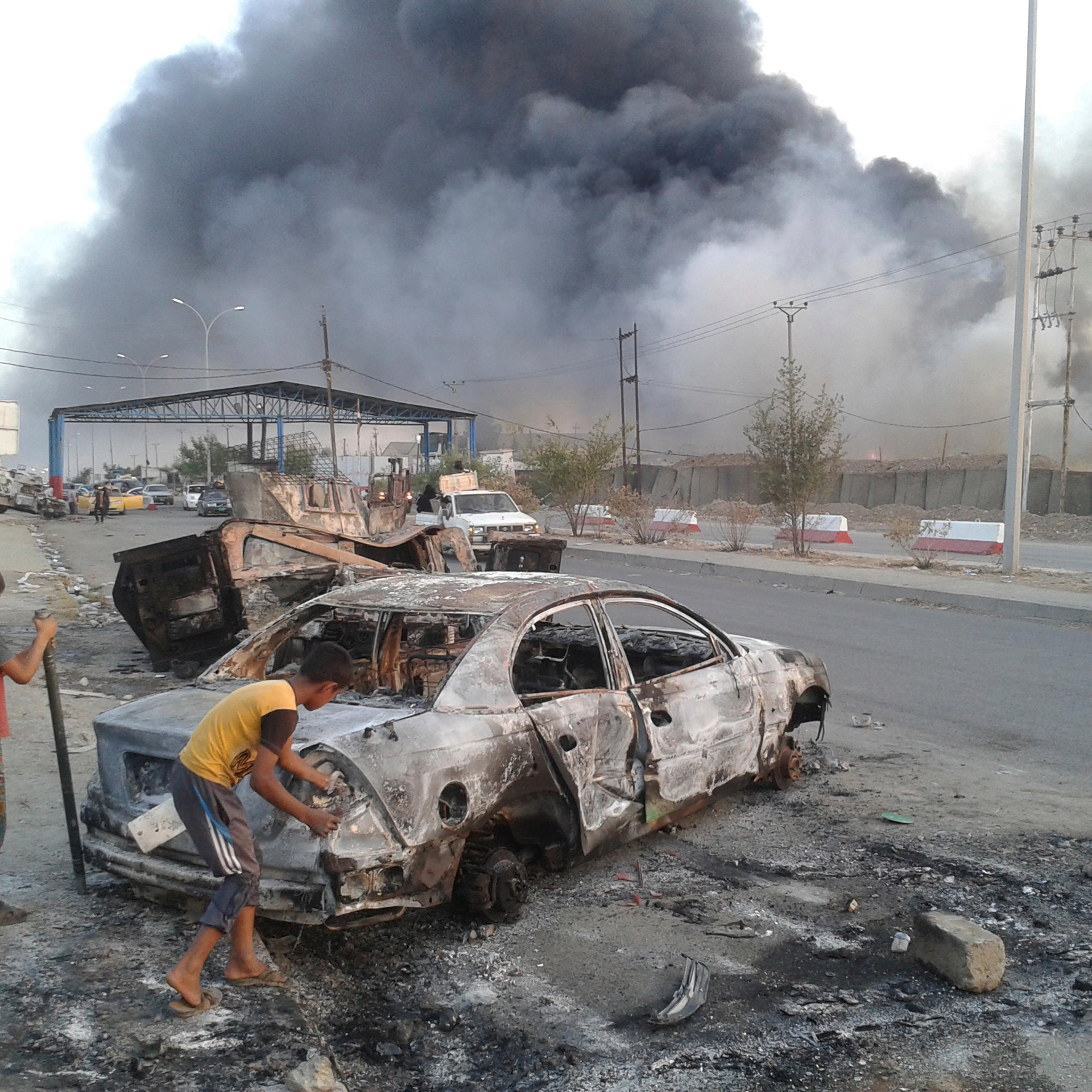Civilian children stand next to a burnt vehicle during clashes between Iraqi security forces and al Qaeda-linked Islamic State in Iraq and the Levant (ISIL) in the northern Iraq city of Mosul