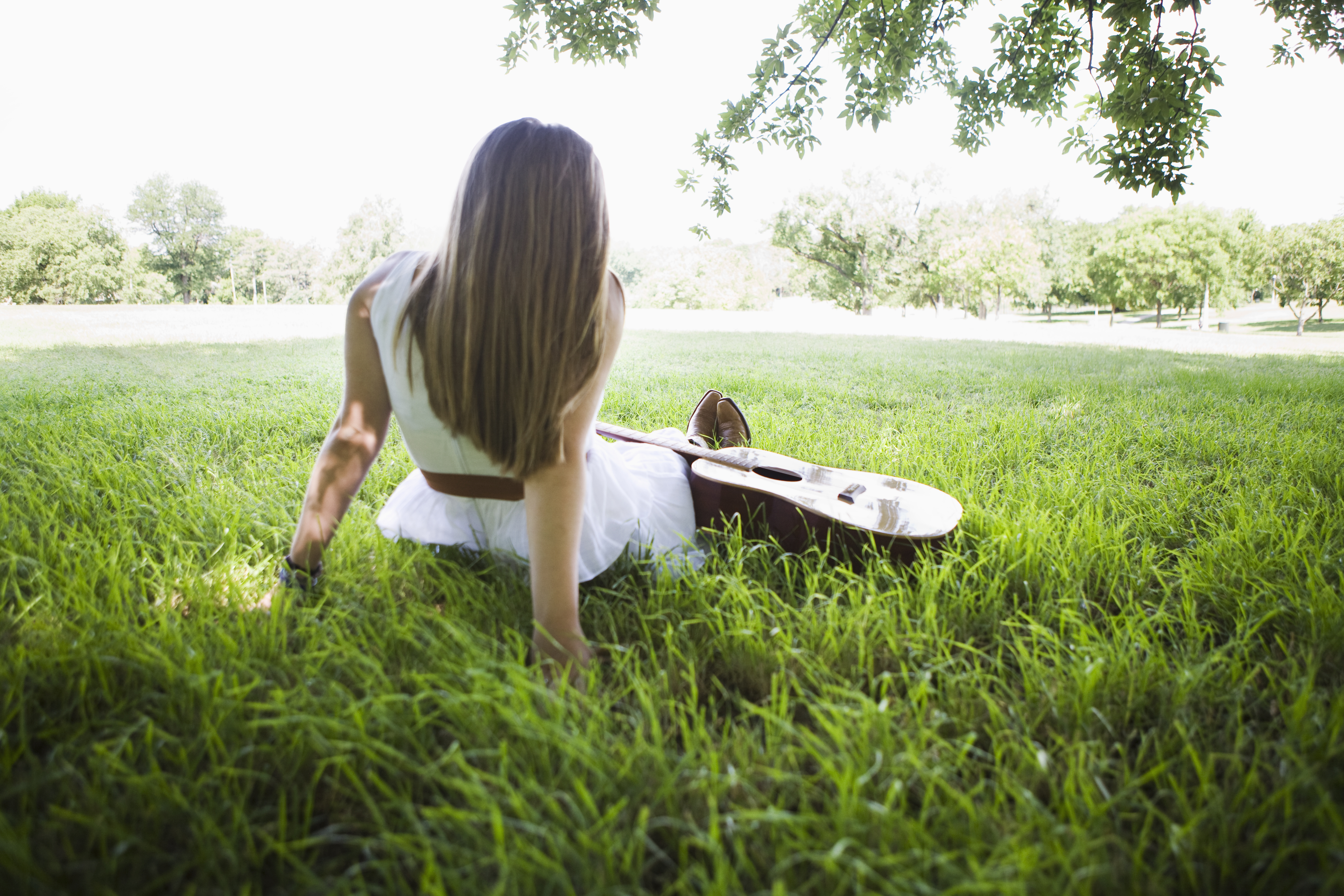 woman-sitting-grass-guitar-rear-view