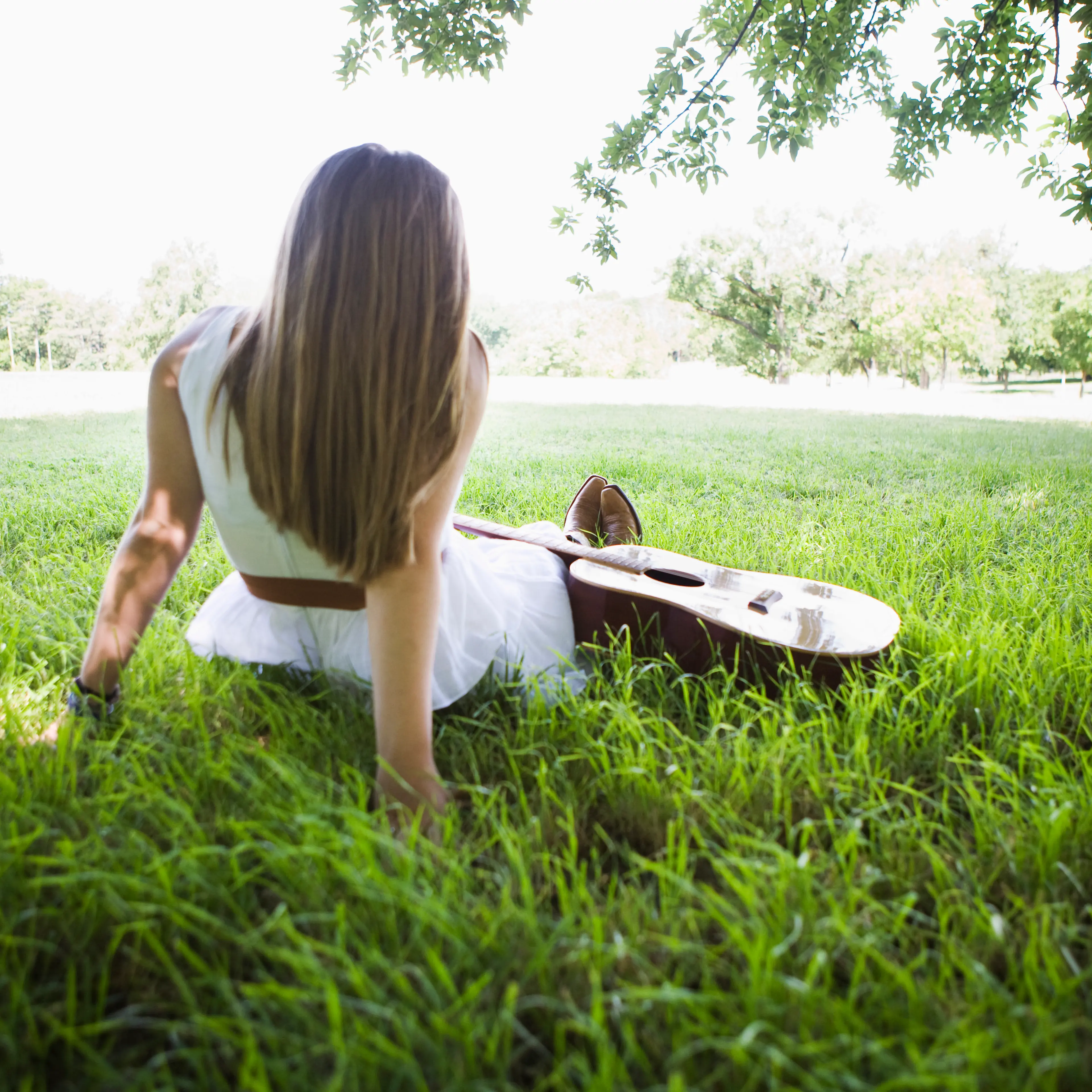woman-sitting-grass-guitar-rear-view