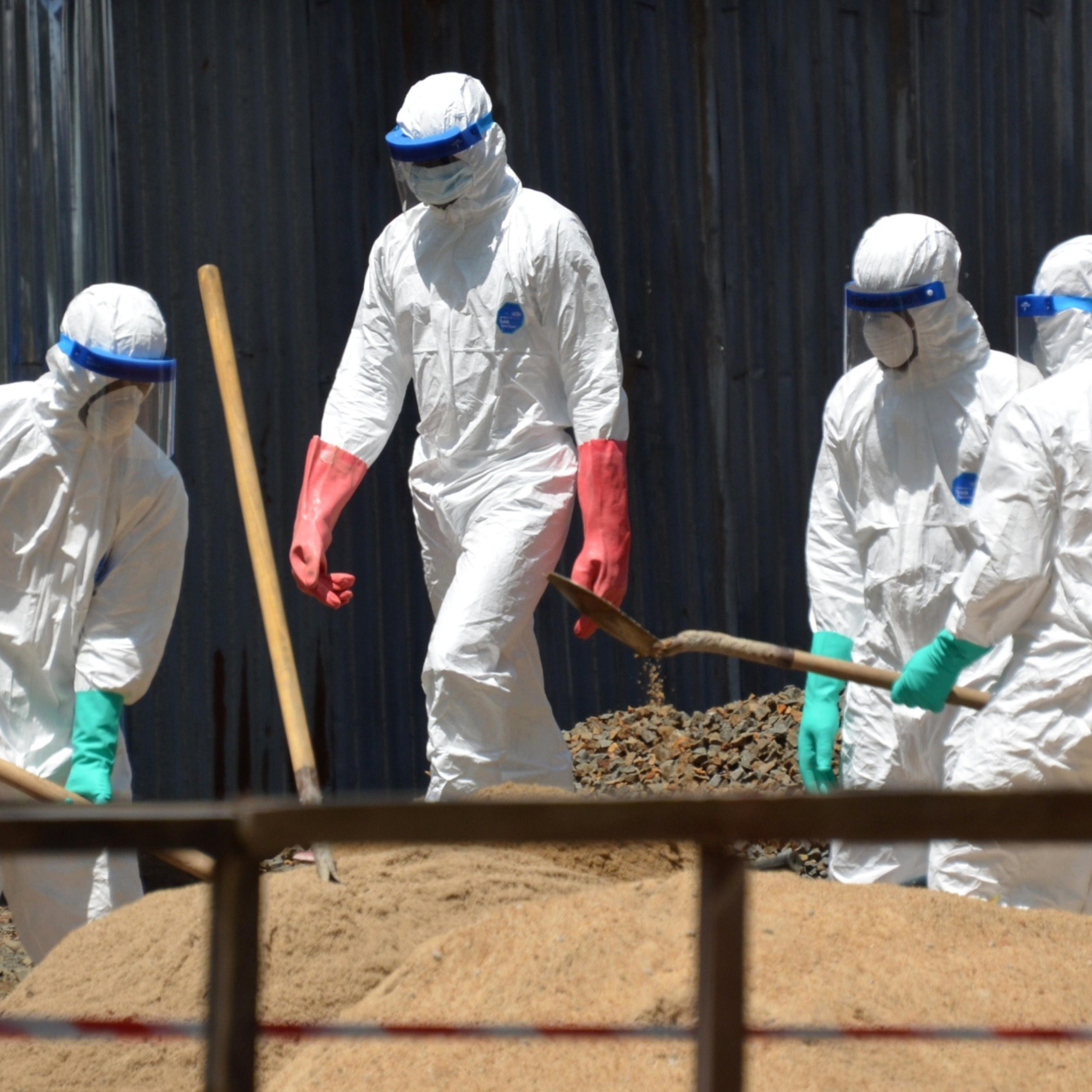 Health workers from the Liberian Red Cross wear protective gear as they shovel sand which will be used to absorb fluids emitted from the bodies of Ebola victims in front of the ELWA 2 Ebola management center in Monrovia on October 23, 2014.