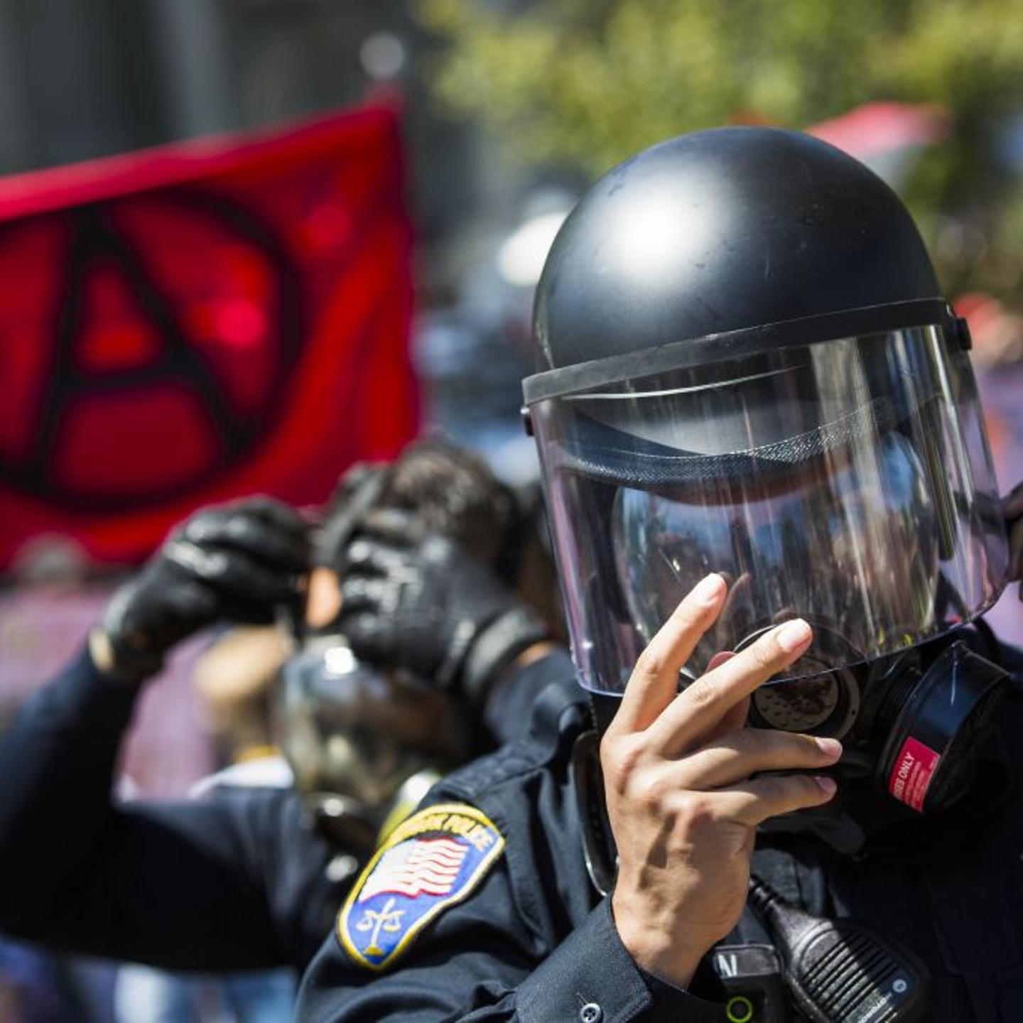 Police officers ready themselves with riot gear and gas masks as protesters holding an anti-fascist flag make their way into Civic Center Park, during demonstrations responding to the cancelled No to Marxism rally, in Berkeley, Calif., on August 27, 2017.