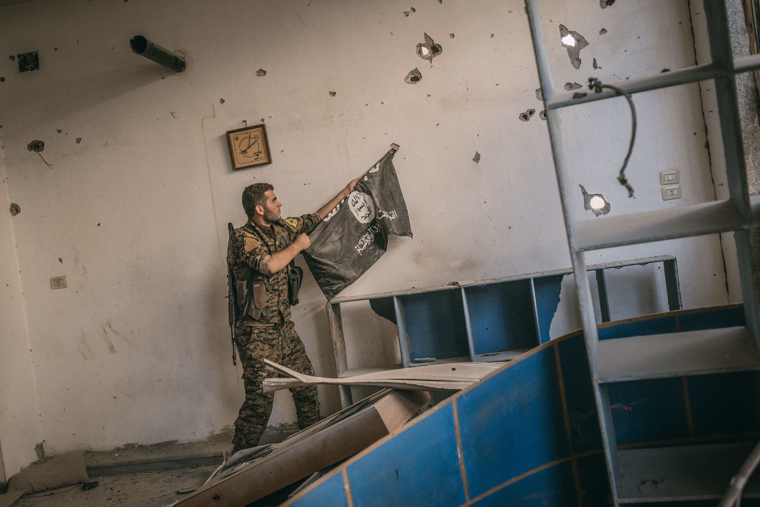 A member of People's Protection Units (YPG), part of the Siria's Democratic Forces, removes an Isis flag from a wall of a building inside Raqqa.