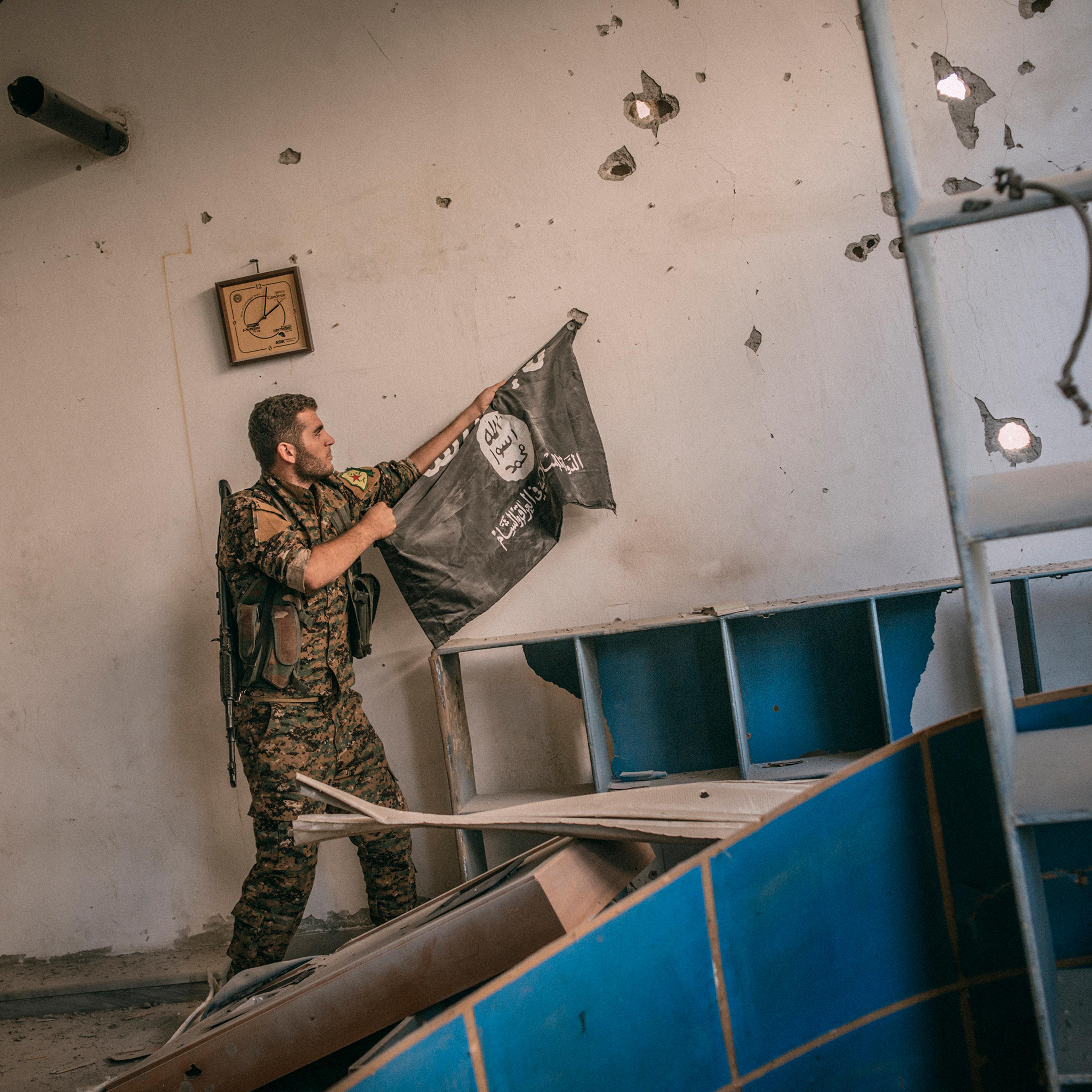 A member of People's Protection Units (YPG), part of the Siria's Democratic Forces, removes an Isis flag from a wall of a building inside Raqqa.