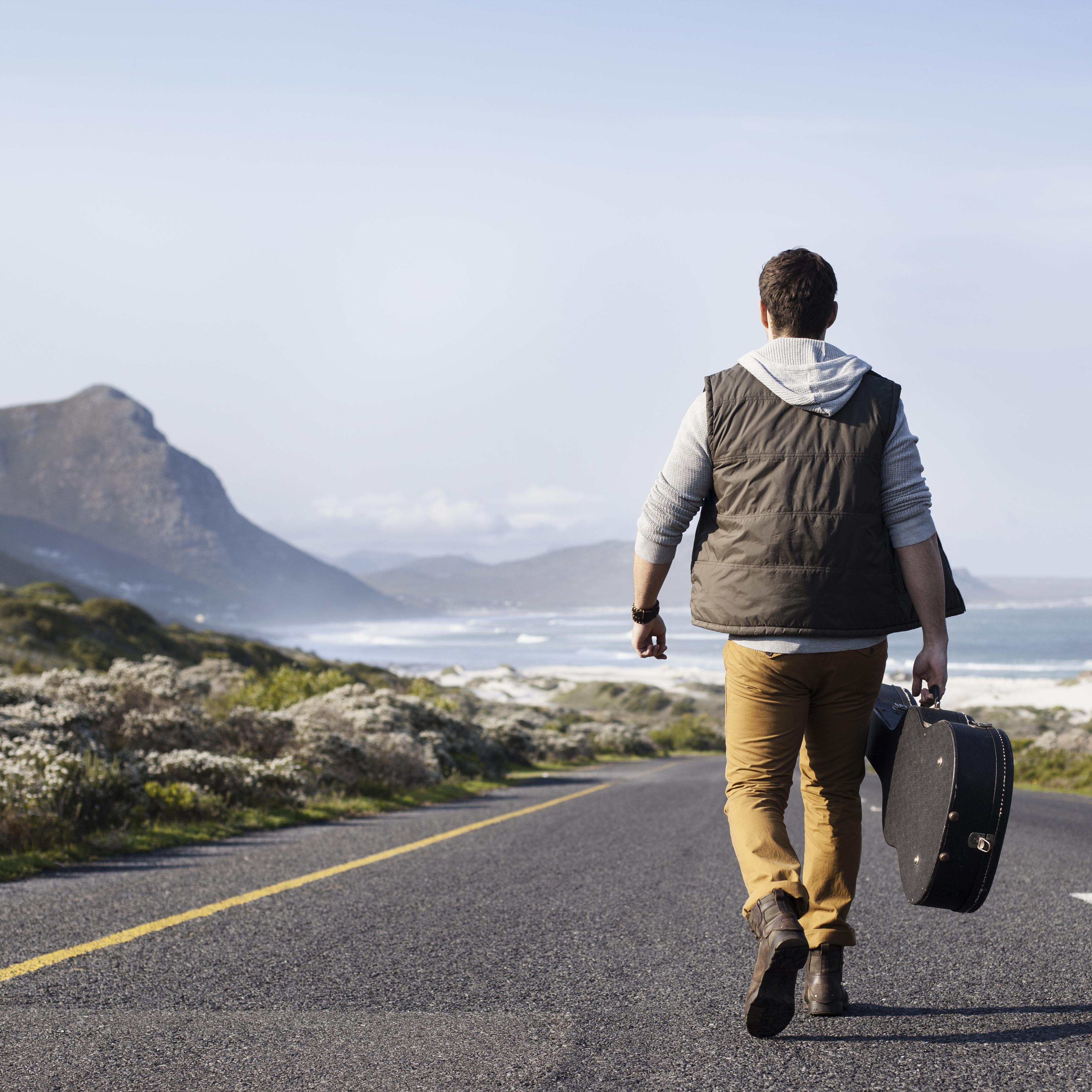 man-walking-road-guitar-rear-view