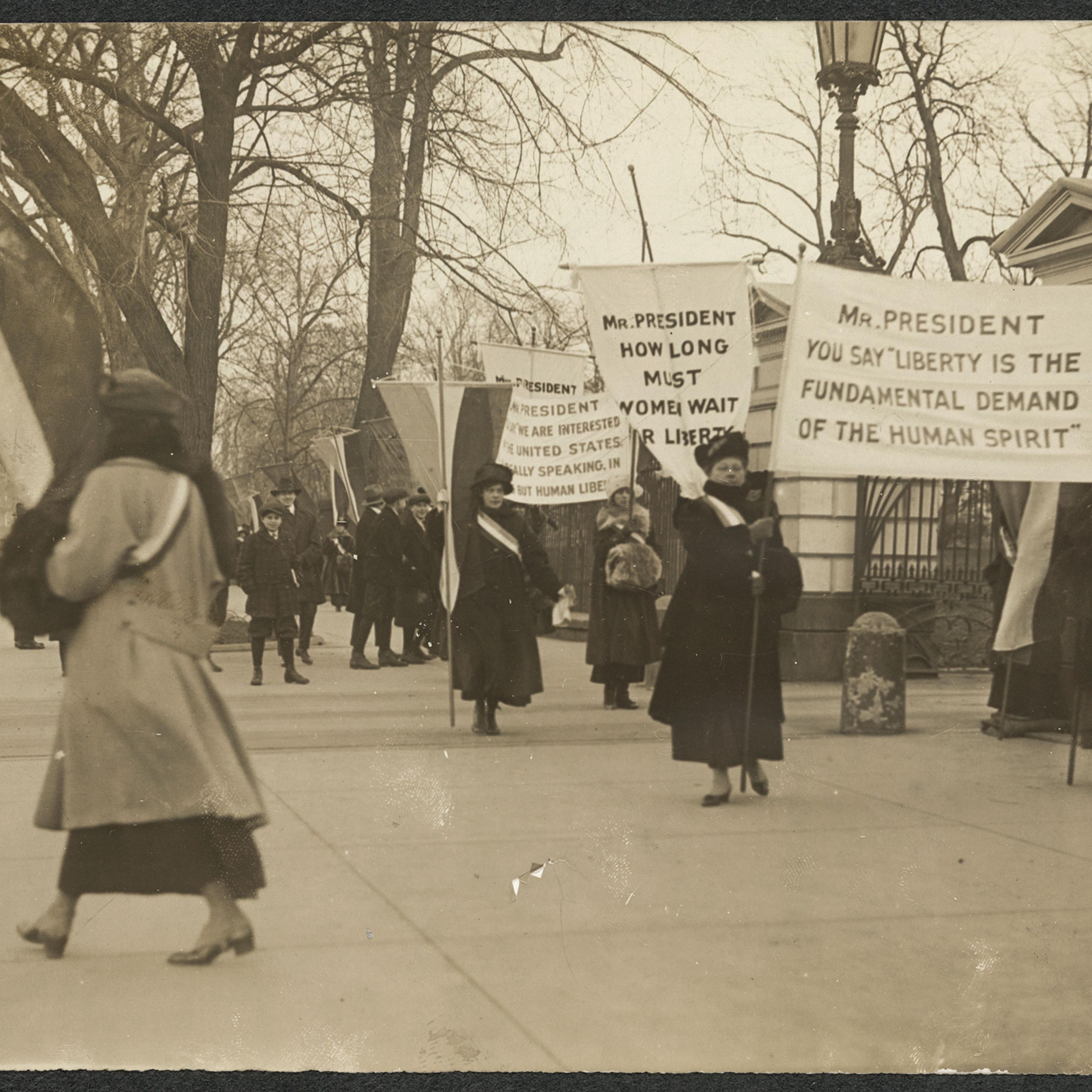 Suffragists picket with banners on the sidewalk in front of White House gates on Jan. 26, 1917.