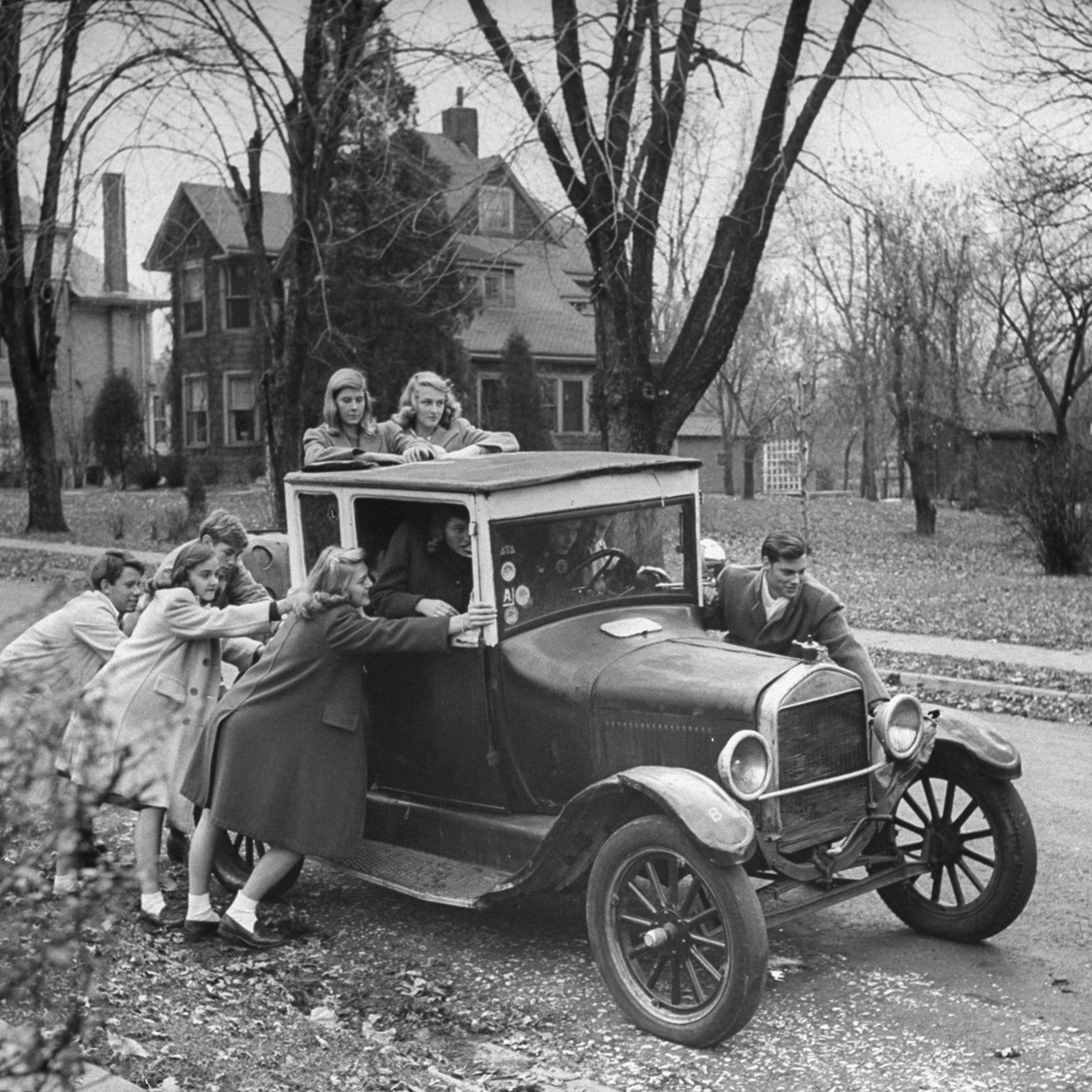 Gang of teen-agers push boyfriend's model T to get it started. Car is 17 years old and can hold 12 boys and girls. Favorite ride is out to football game.
