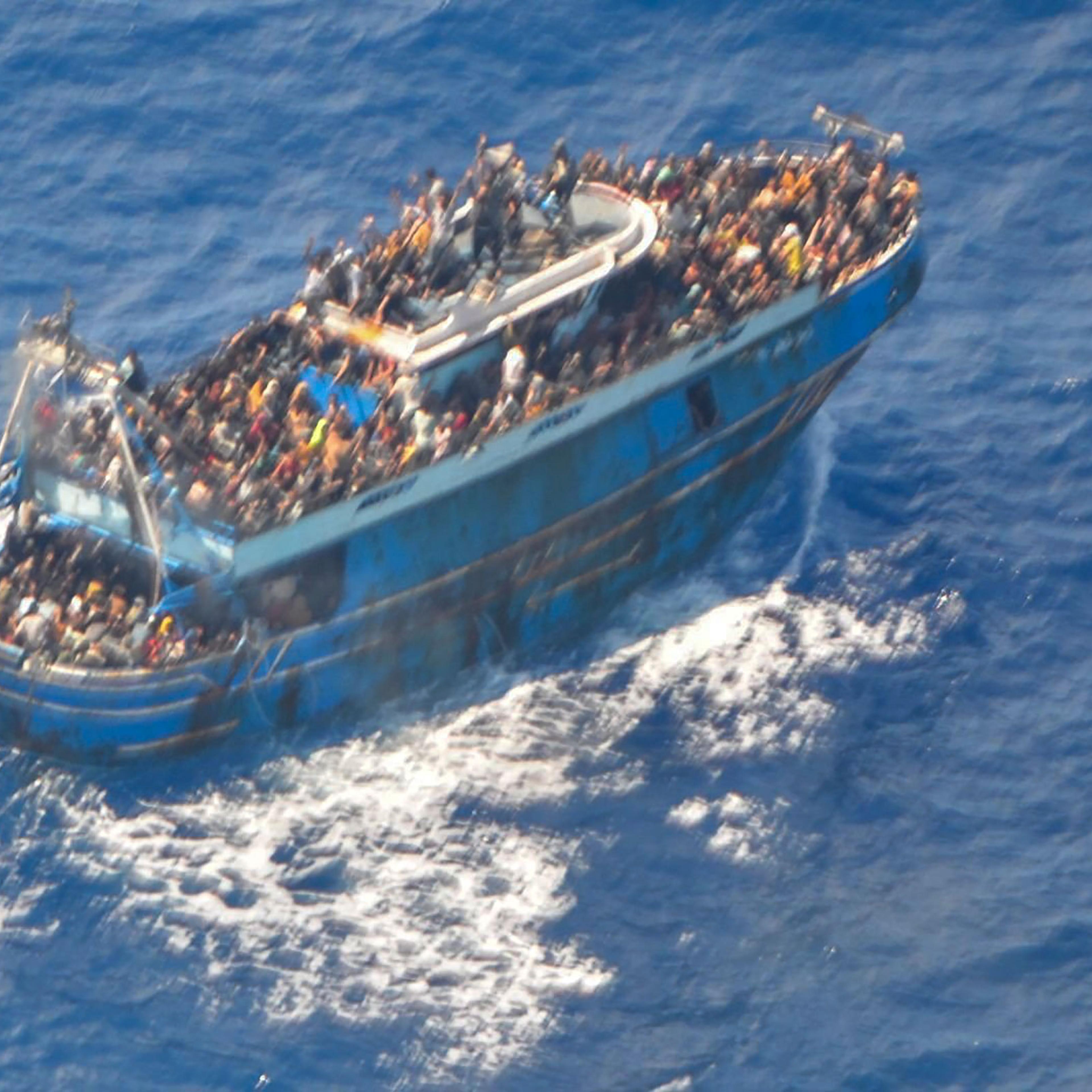 A grainy photograph that shows a large blue battered fishing boat in the ocean filled with people