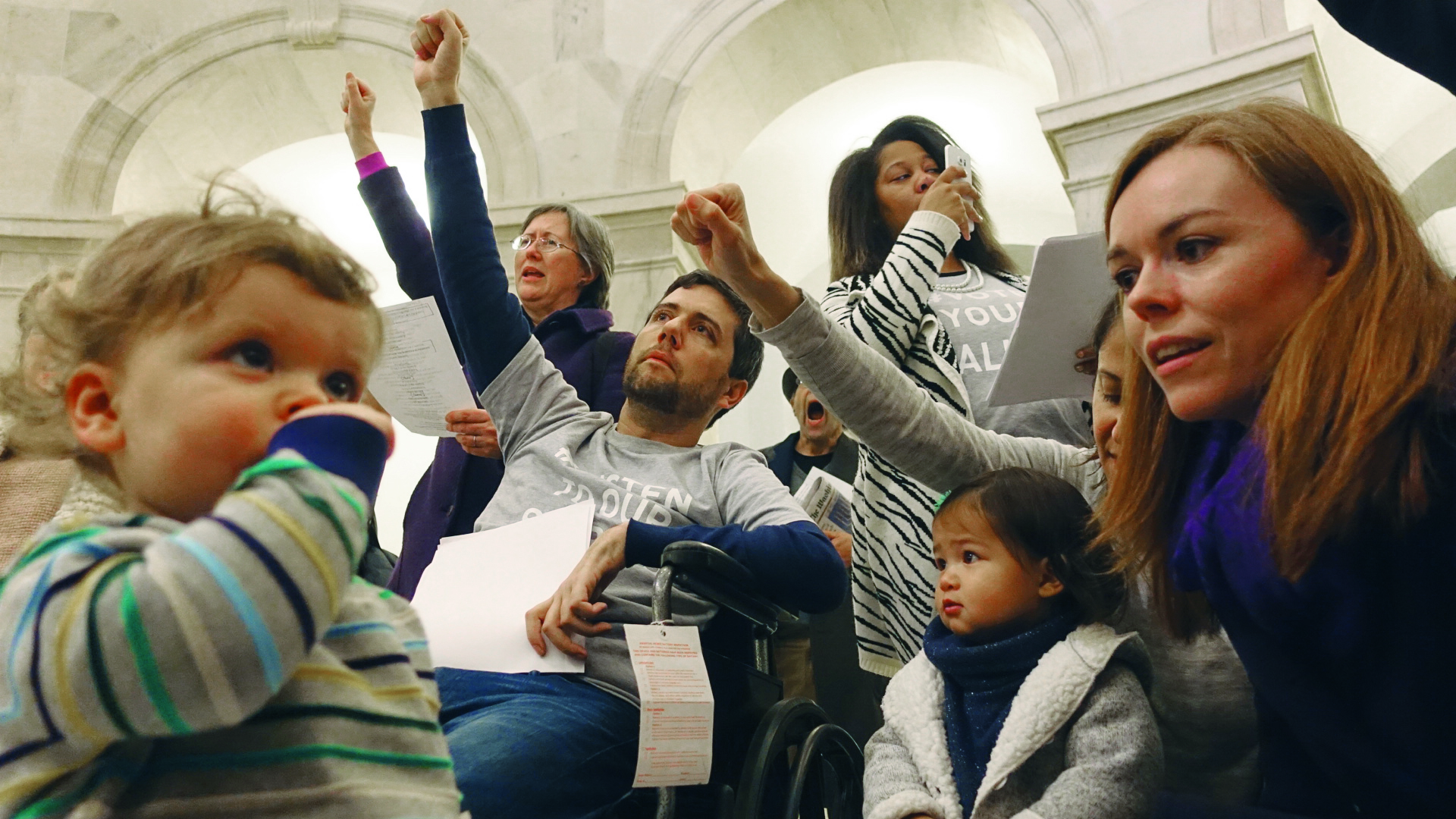 Ady Barkan sings "This Land Is Your Land" in the rotunda of the Russell Senate Office Building with his son Carl, wife Rachael and friends.