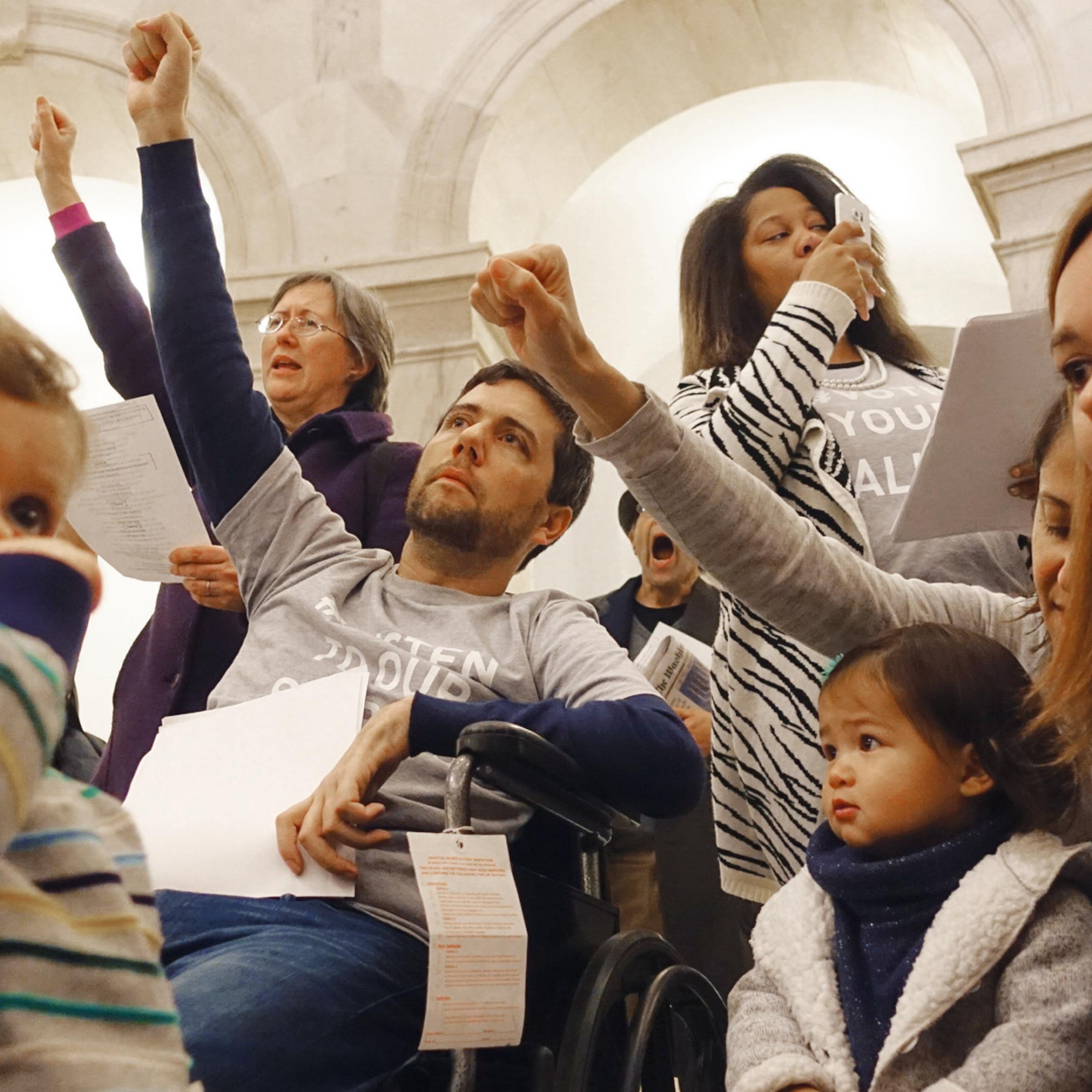 Ady Barkan sings "This Land Is Your Land" in the rotunda of the Russell Senate Office Building with his son Carl, wife Rachael and friends.